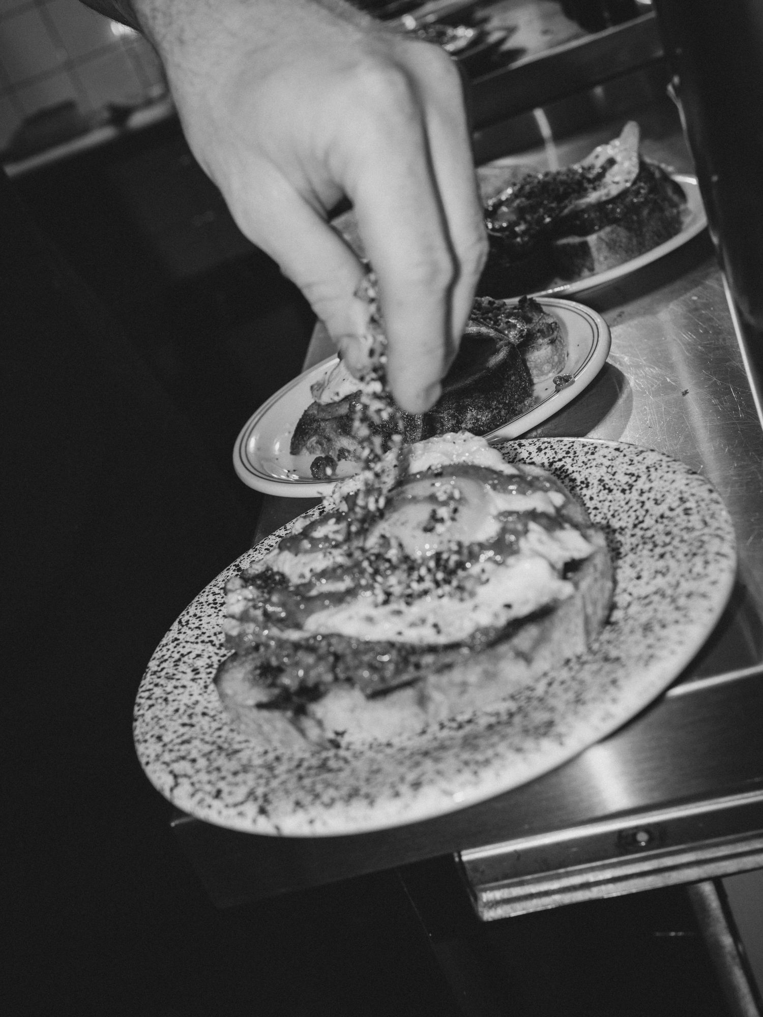 Chef sprinkling seasoning on a plated dish in a professional kitchen.