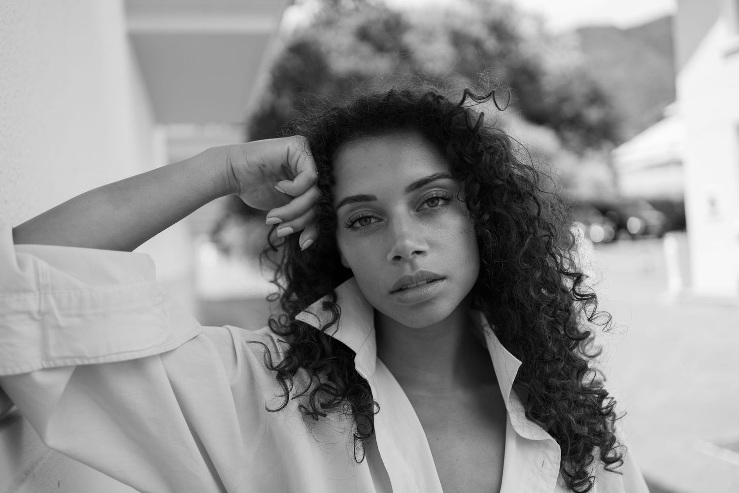 Black and white portrait of a young woman with curly hair posing outdoors in a white shirt.