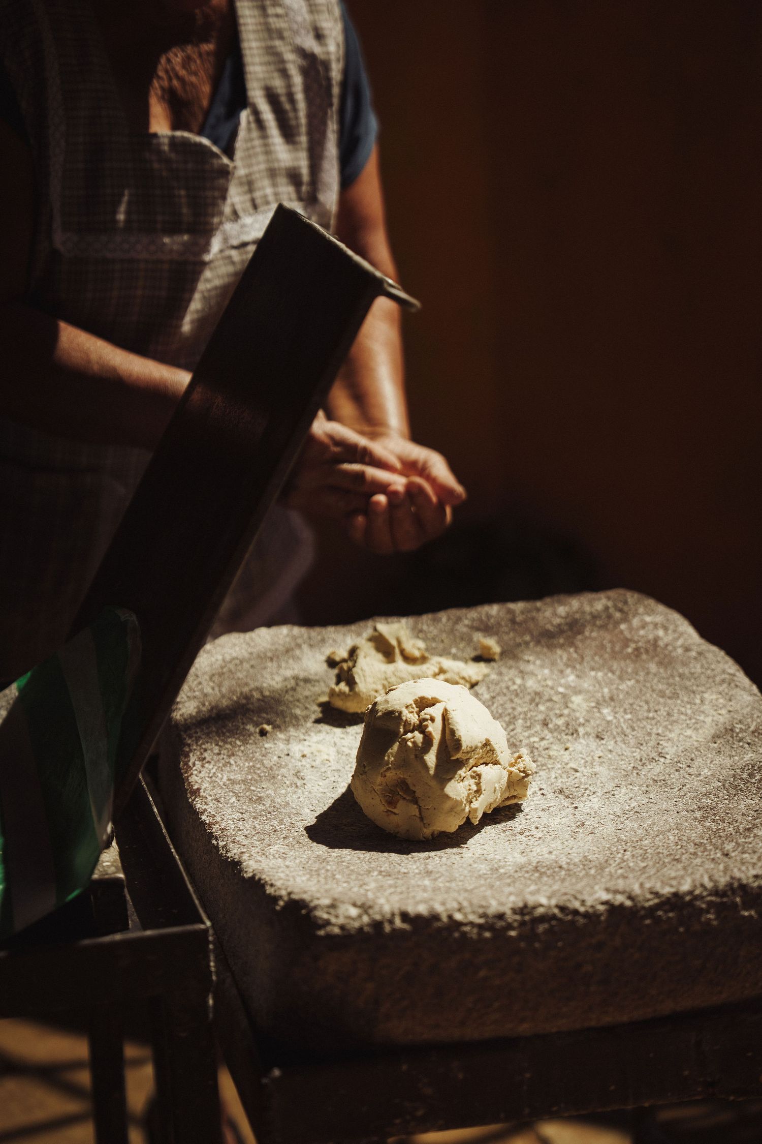 Person crushing garlic on a stone surface with a large knife in rustic kitchen setting.