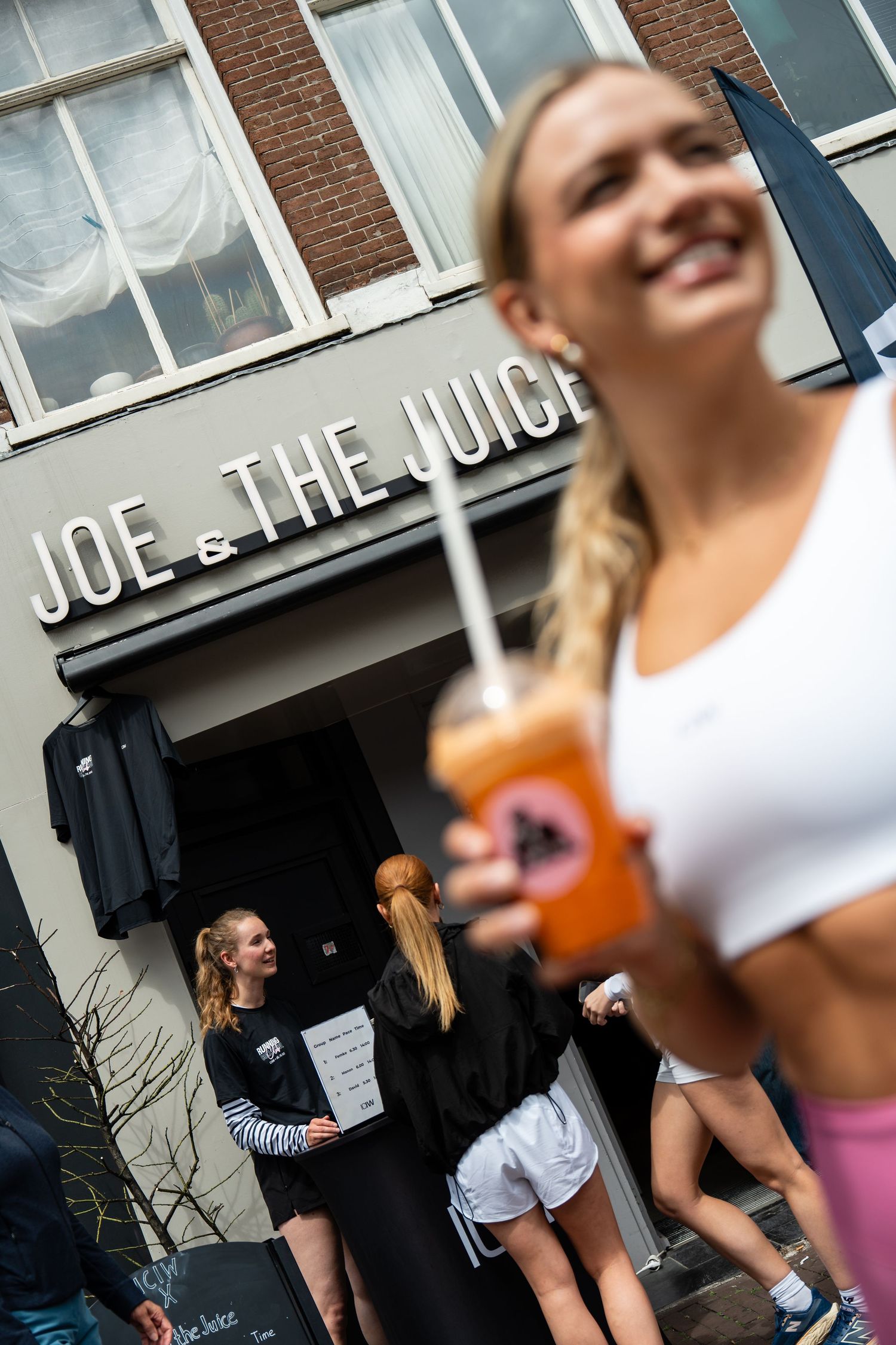 Smiling blonde woman holding a fresh juice outside Joe & The Juice store in Amsterdam.