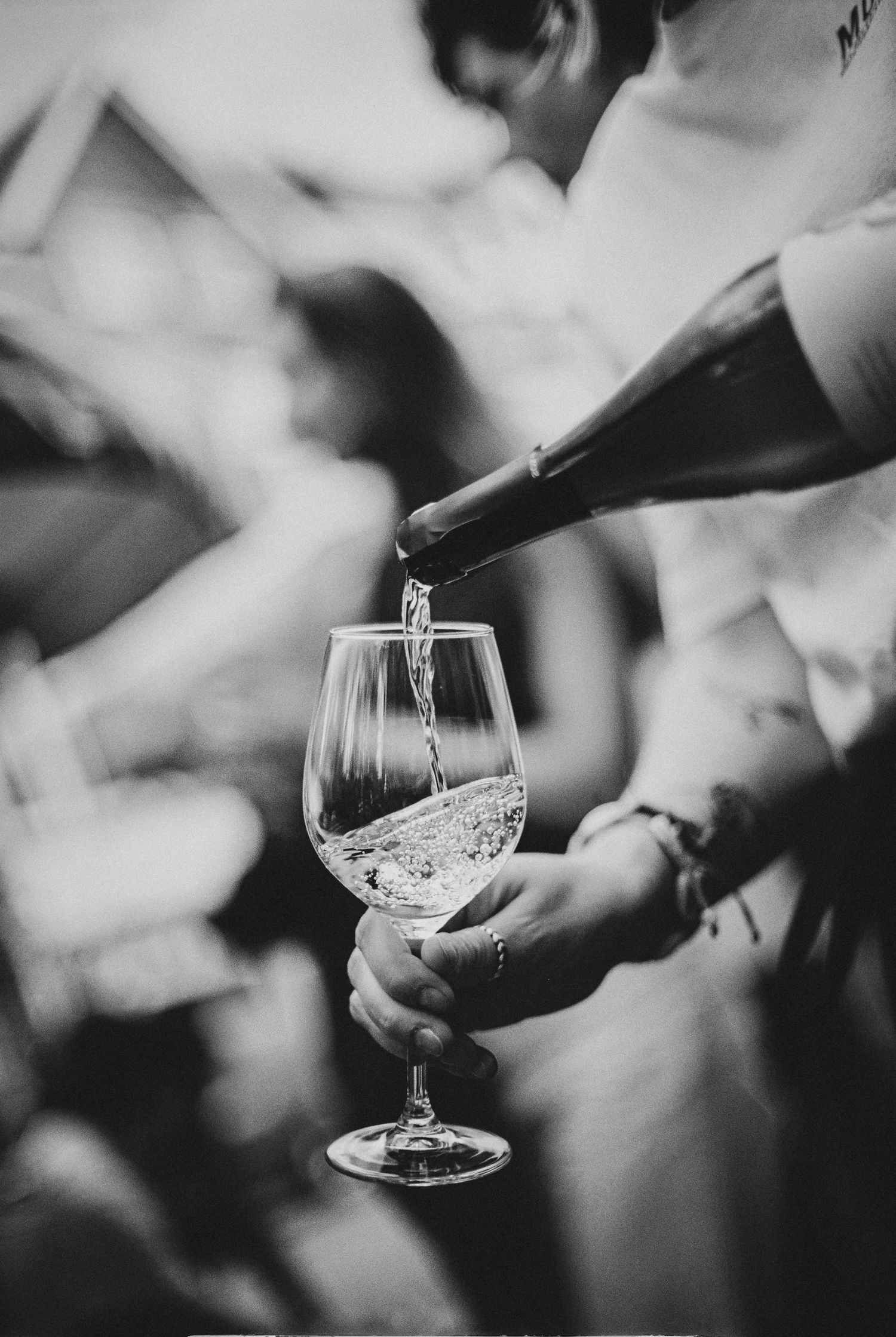 Black and white photo of a person pouring white wine from a bottle into an elegant wine glass.