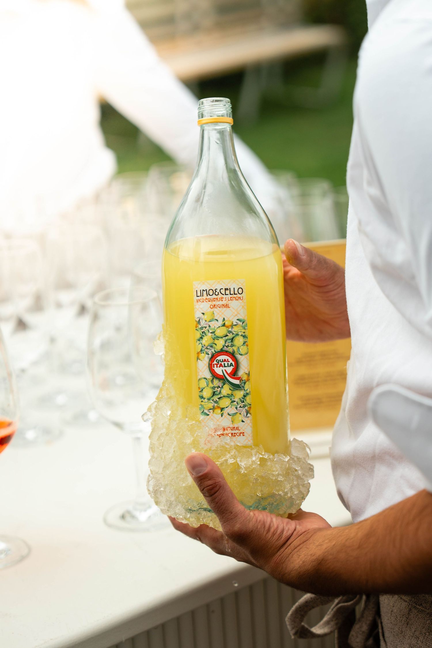Person holding a large bottle of Limoncello liqueur wrapped in ice at an outdoor event.