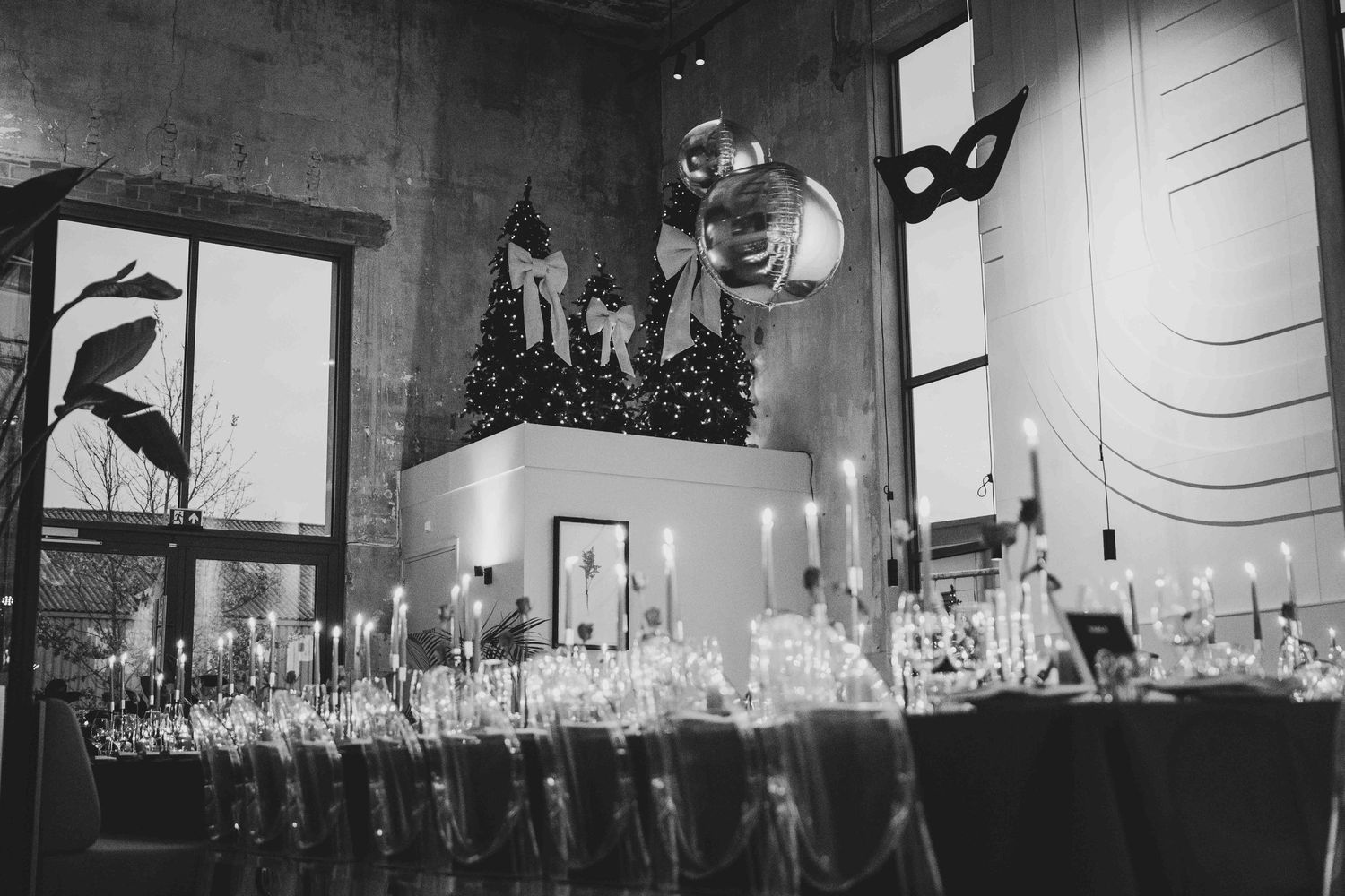 Black and white photo of an elegant event setup with candles, balloons, and a decorated Christmas tree centerpiece.