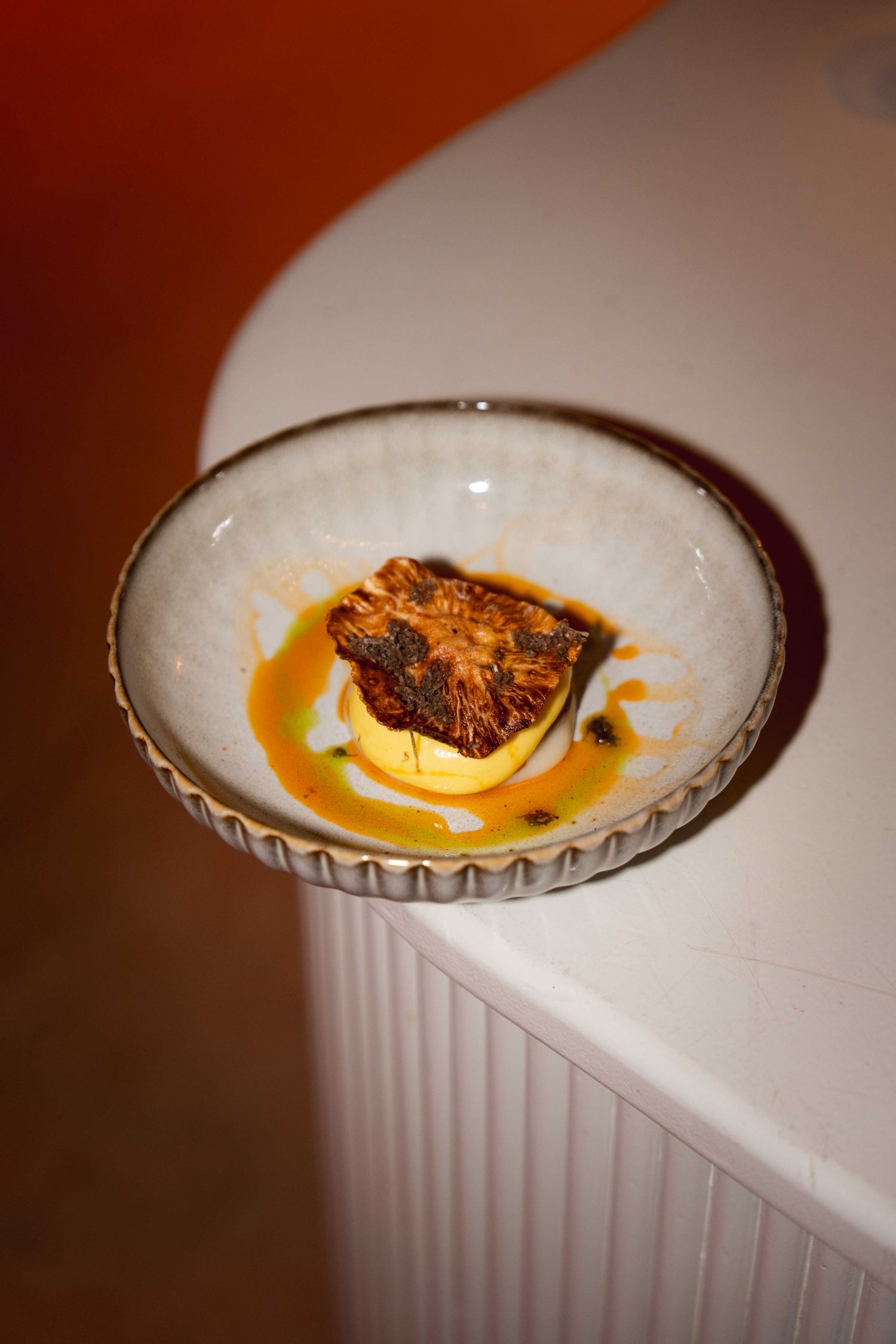 Elegant ceramic bowl with caramelized pineapple slice in golden sauce, served on white surface.