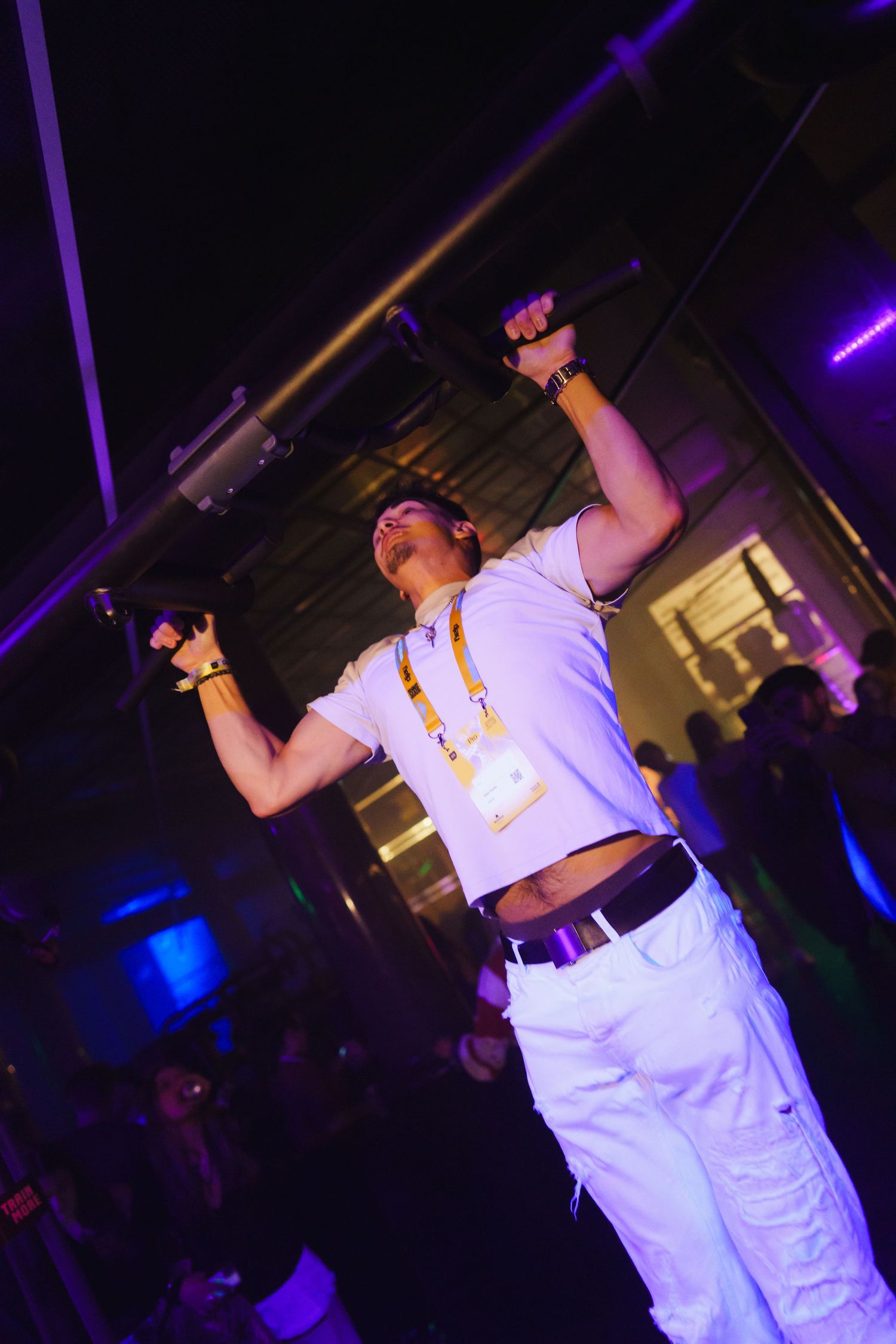 Man in white outfit performing pull-ups under purple club lights.