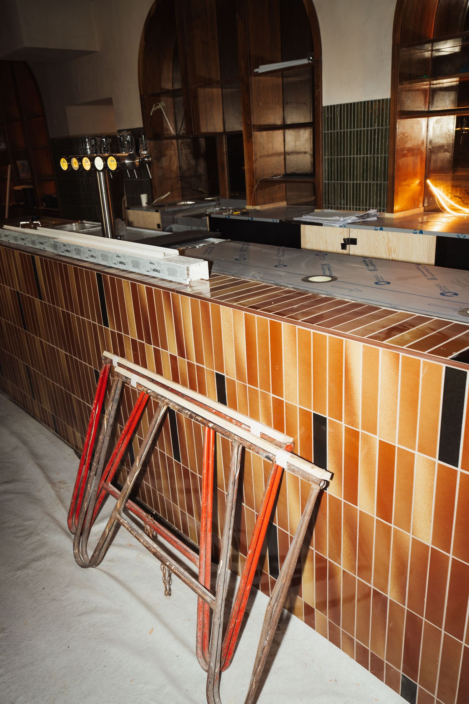 Bar counter with colorful striped tiles, beer taps, and a red wooden sawhorse in a renovated restaurant interior.