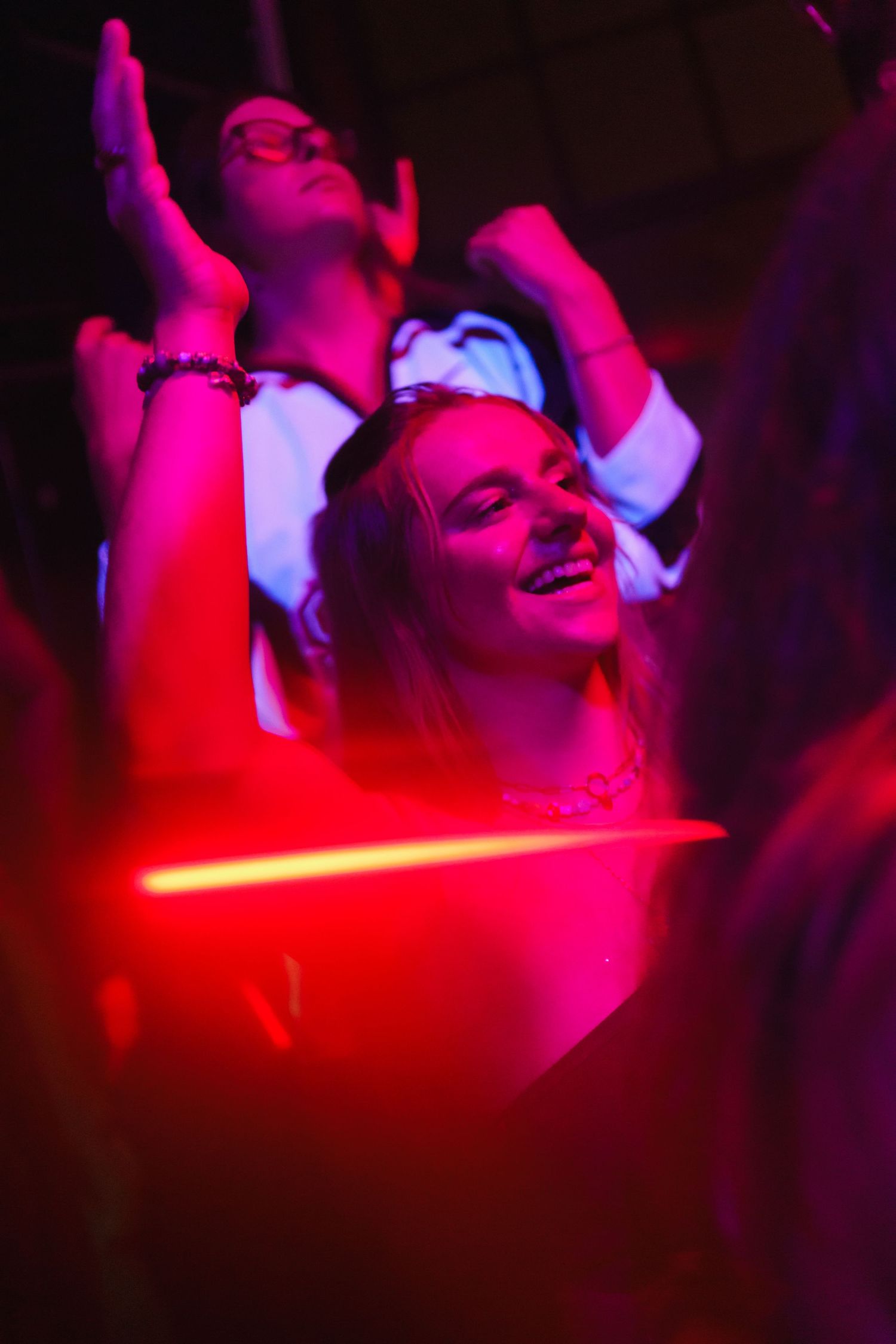 Young woman smiling and dancing under pink and red neon lights at a lively nightclub event.