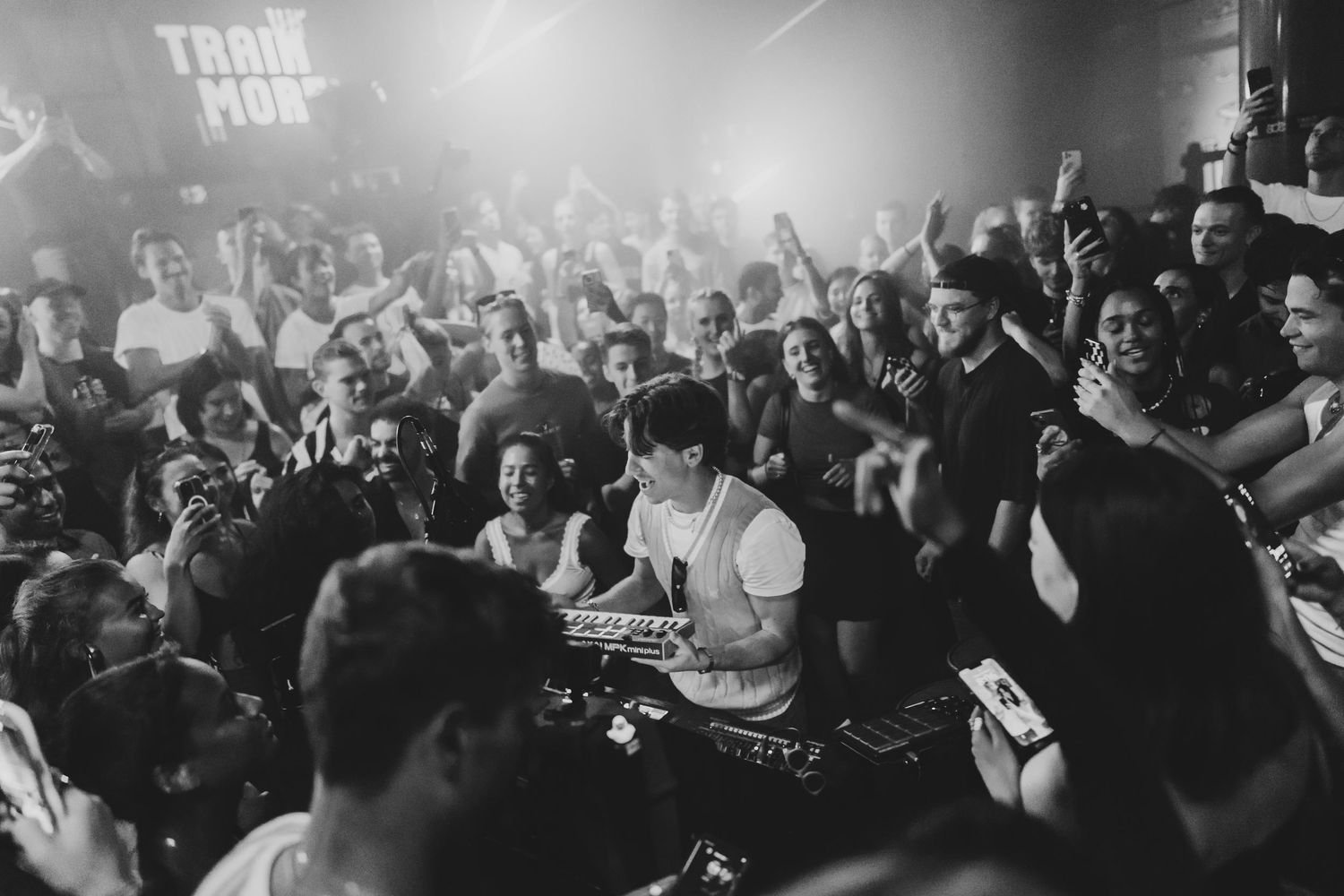 DJ performing at packed nightclub party with crowd cheering in black and white photo.