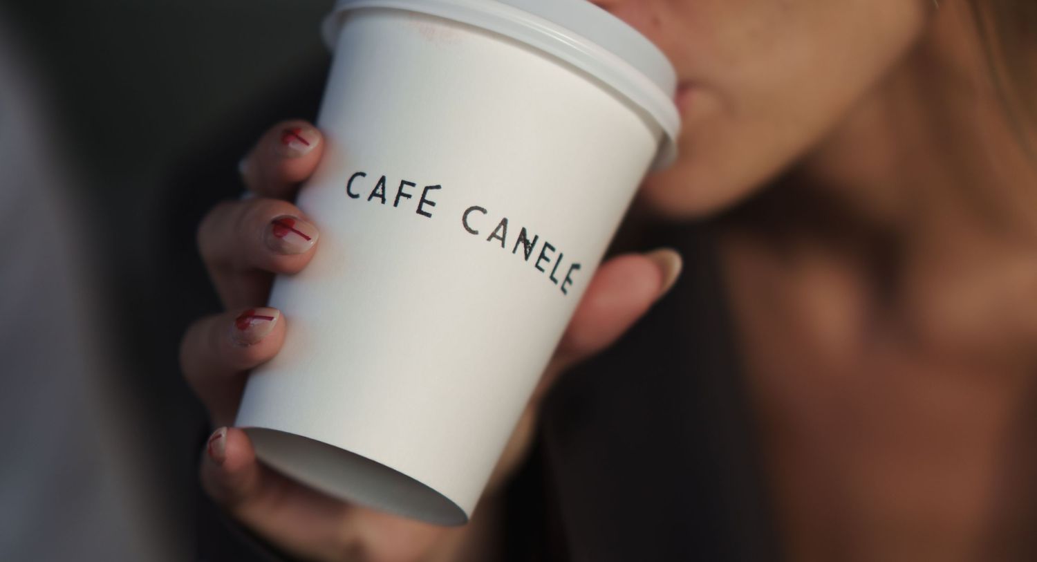 A person sipping coffee from a white Cafe Canele paper cup.