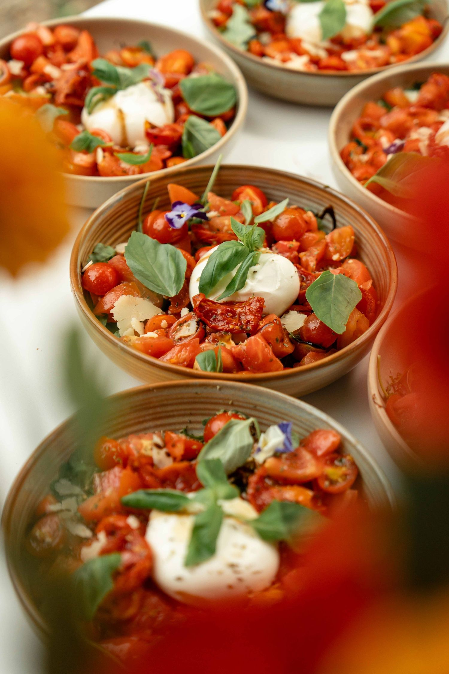 Multiple ceramic bowls filled with fresh tomato bruschetta topped with mozzarella and basil leaves served at a catered event.