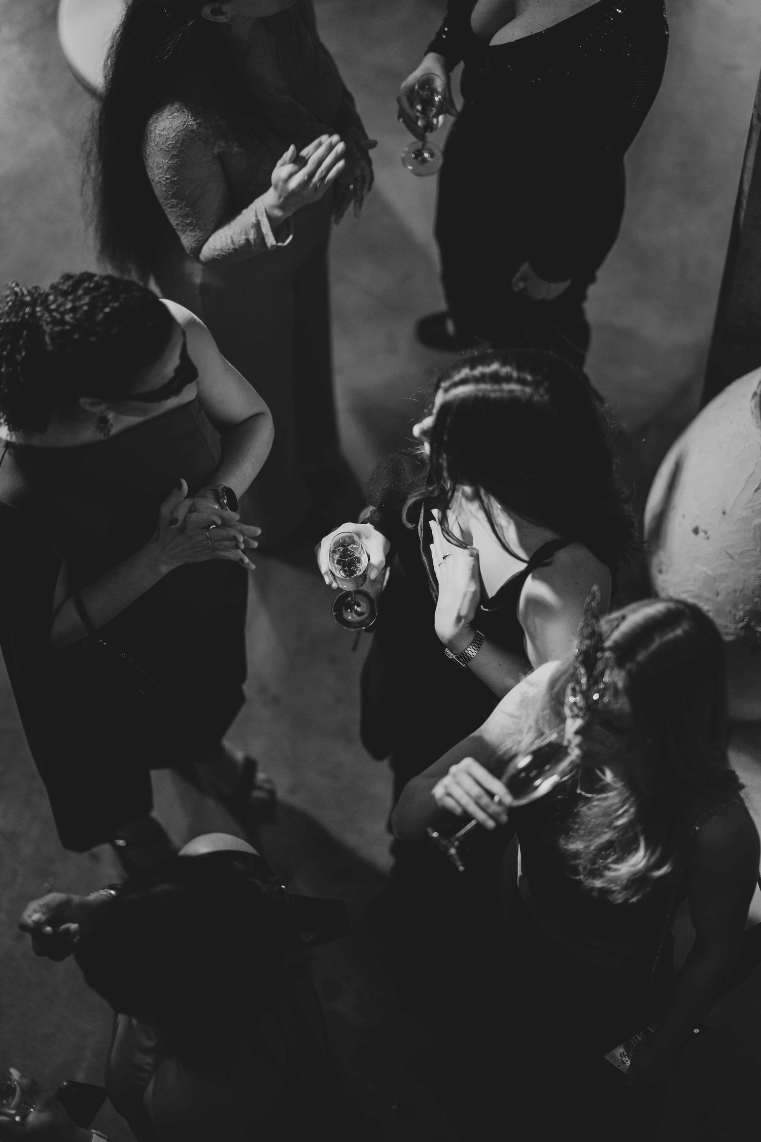 Overhead black and white view of elegantly dressed guests mingling and holding champagne glasses at a formal event.