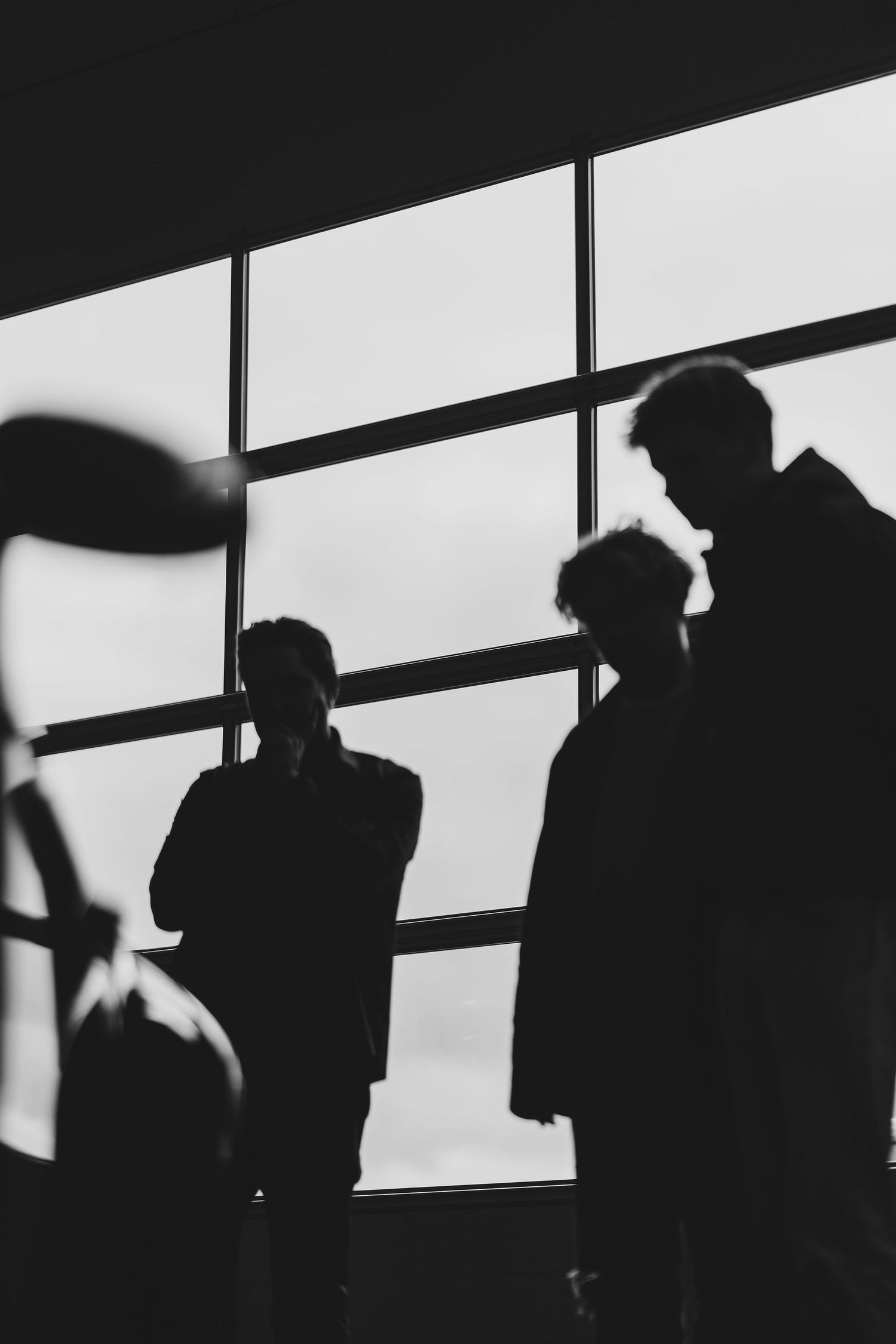 Black and white silhouettes of three people conversing near large windows in a modern building.