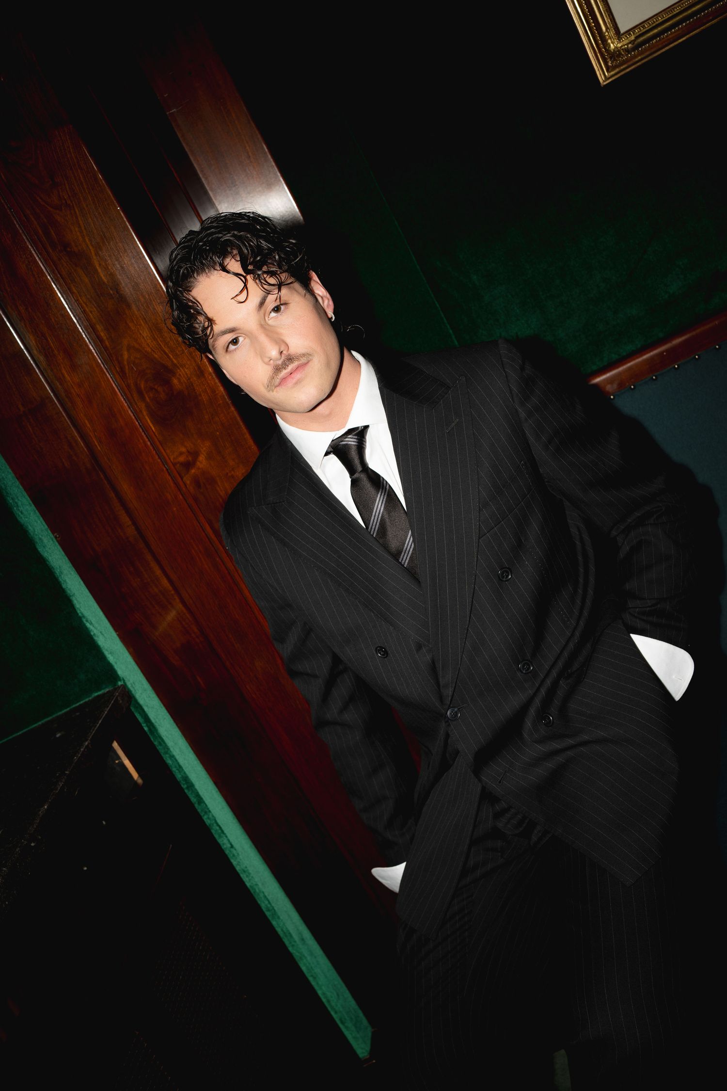 Stylish man in pinstripe suit and tie posing confidently in an elegant dark wood interior.