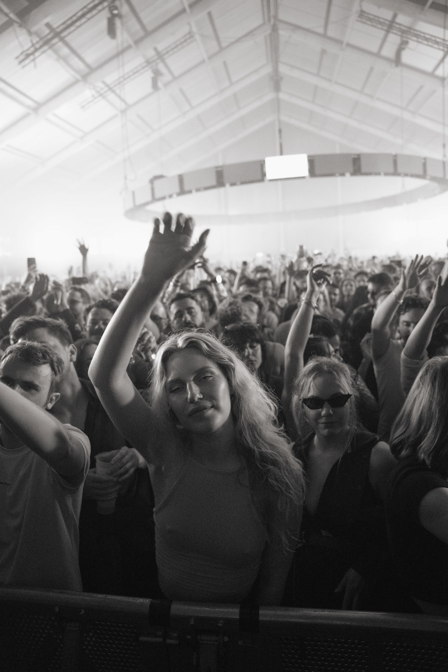 Black and white photo of a crowd at a concert, with a young woman raising her hand in the foreground.