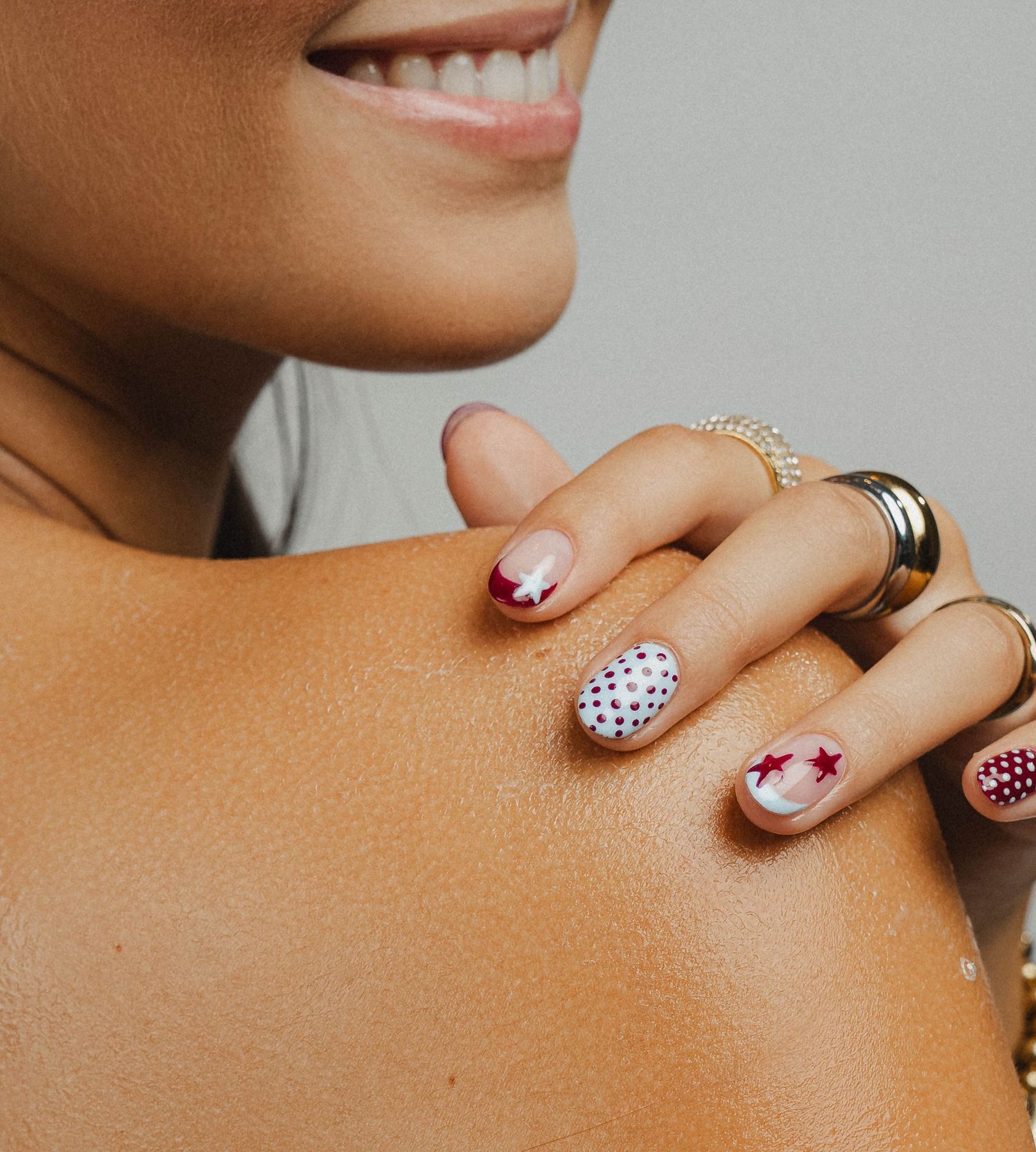 Close-up of manicured nails featuring star and polka dot nail art designs in red and navy on a smiling woman.