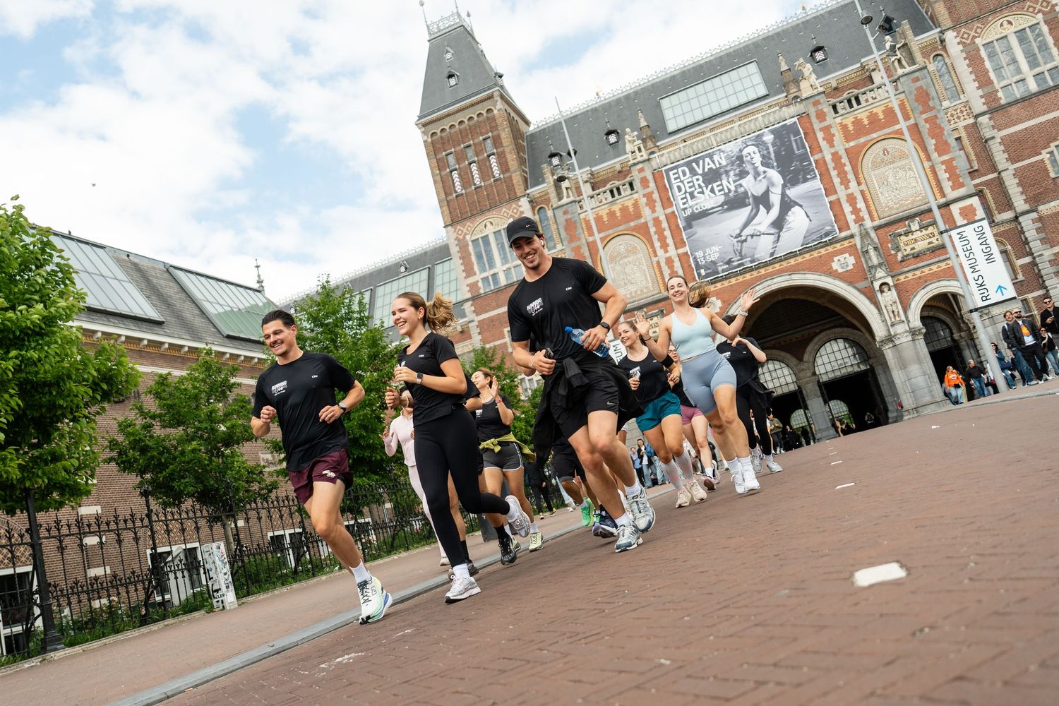 Group of runners jogging past the Rijksmuseum in Amsterdam on a cloudy day.