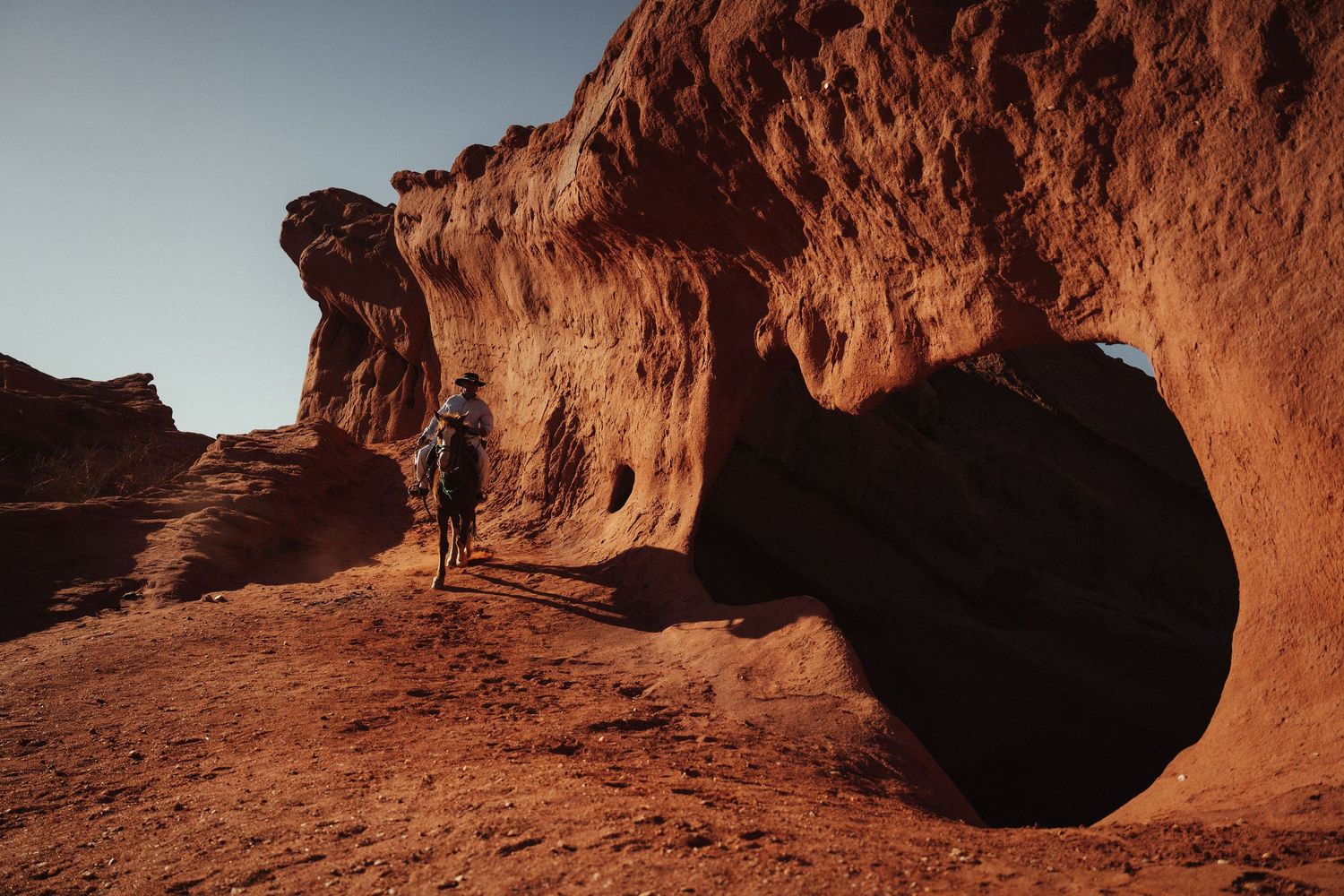 Hiker exploring red sandstone rock formations in a desert canyon landscape under clear blue sky.