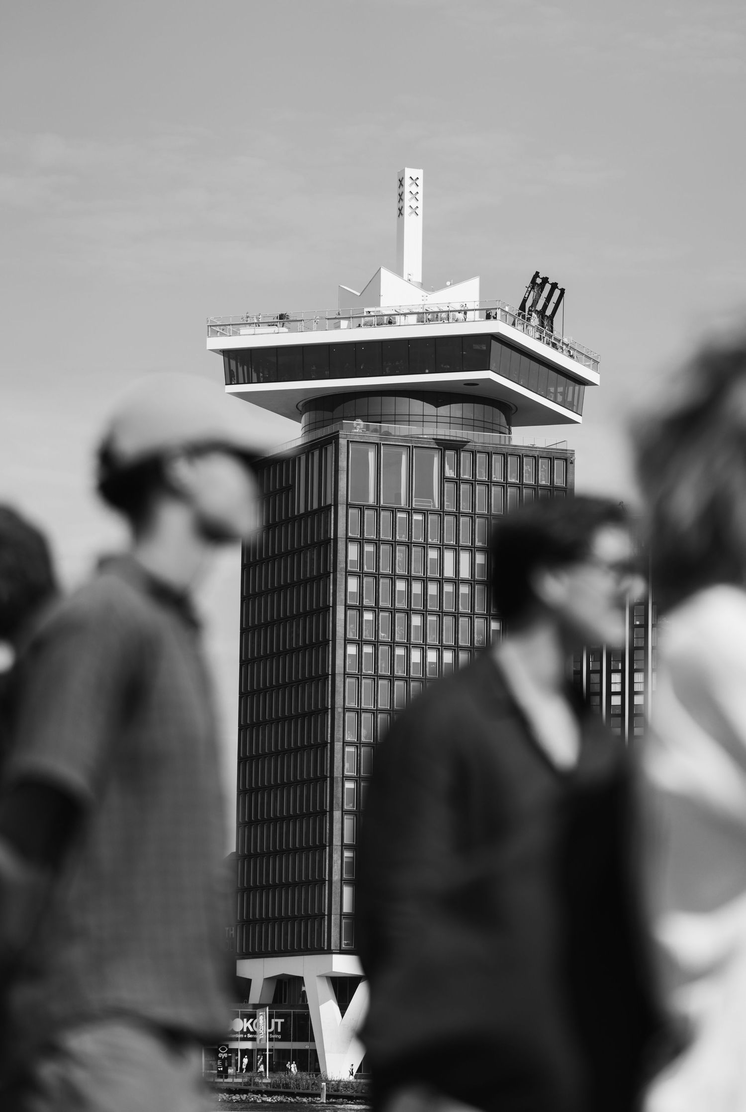 Black and white photo of the A'DAM Tower in Amsterdam with blurred pedestrians in the foreground.