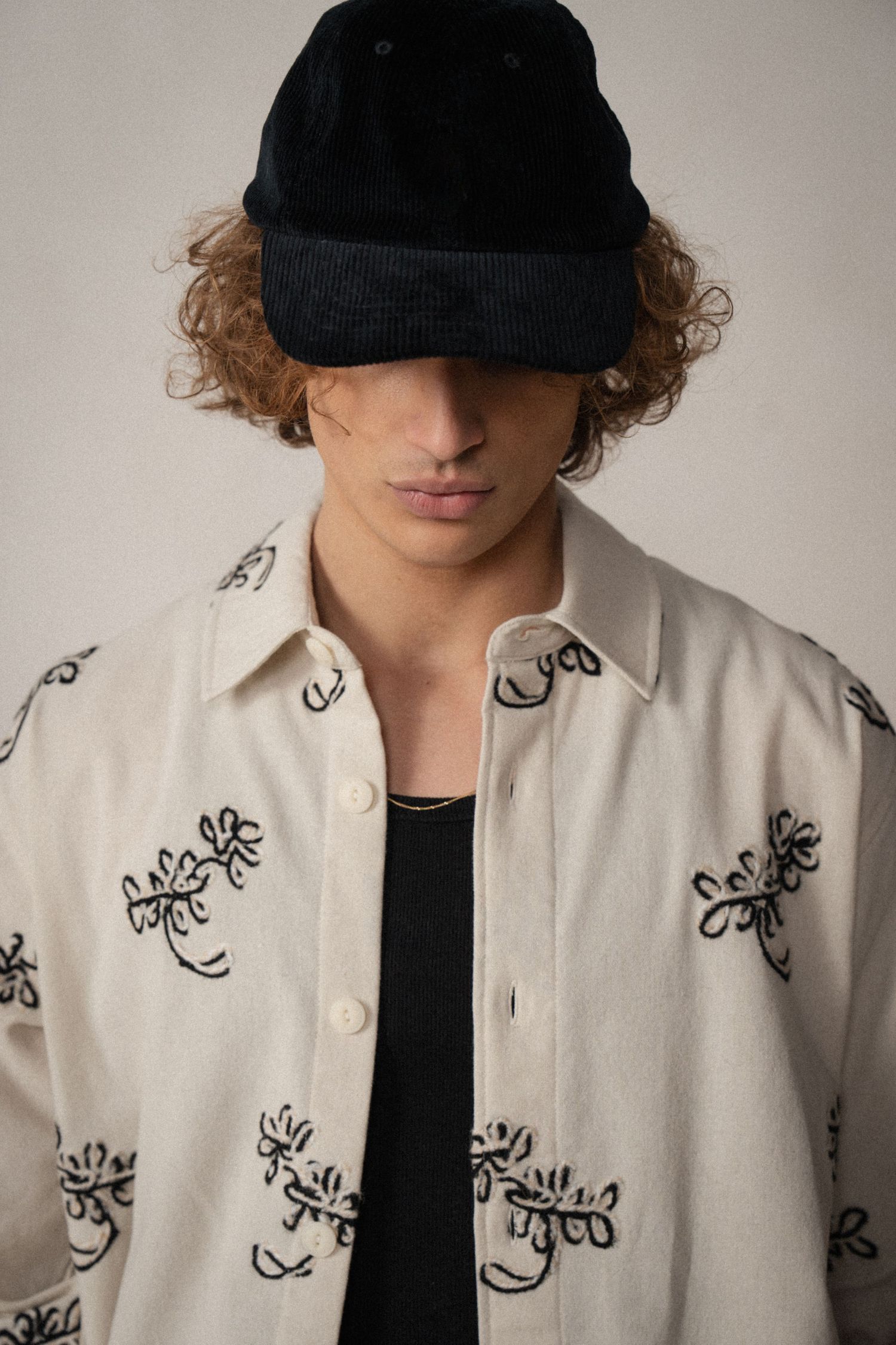 A series of fashion photos showing a white embroidered jacket with black floral designs worn with a black cap.