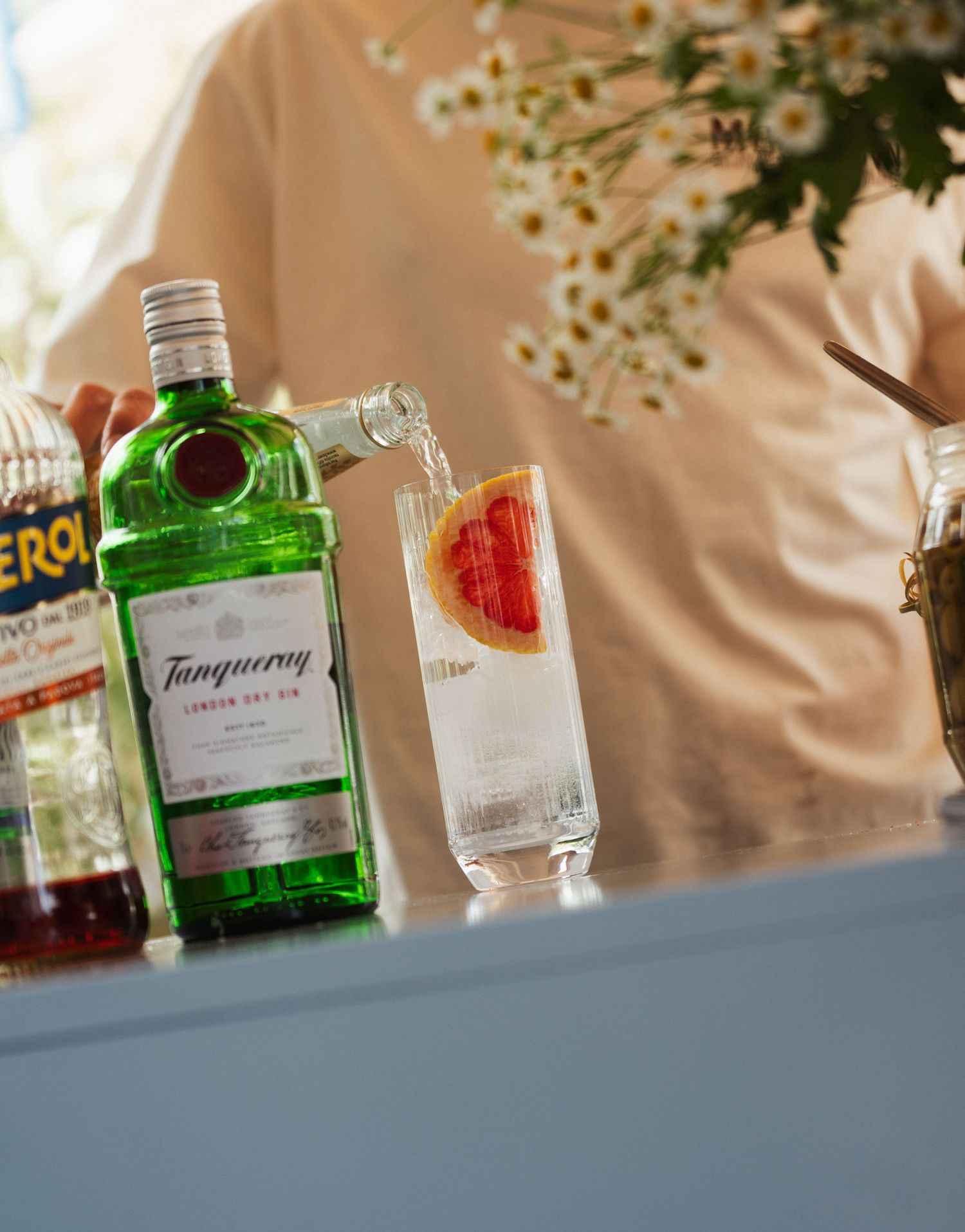 Tanqueray London Dry Gin being poured into a tall glass with grapefruit slice garnish.