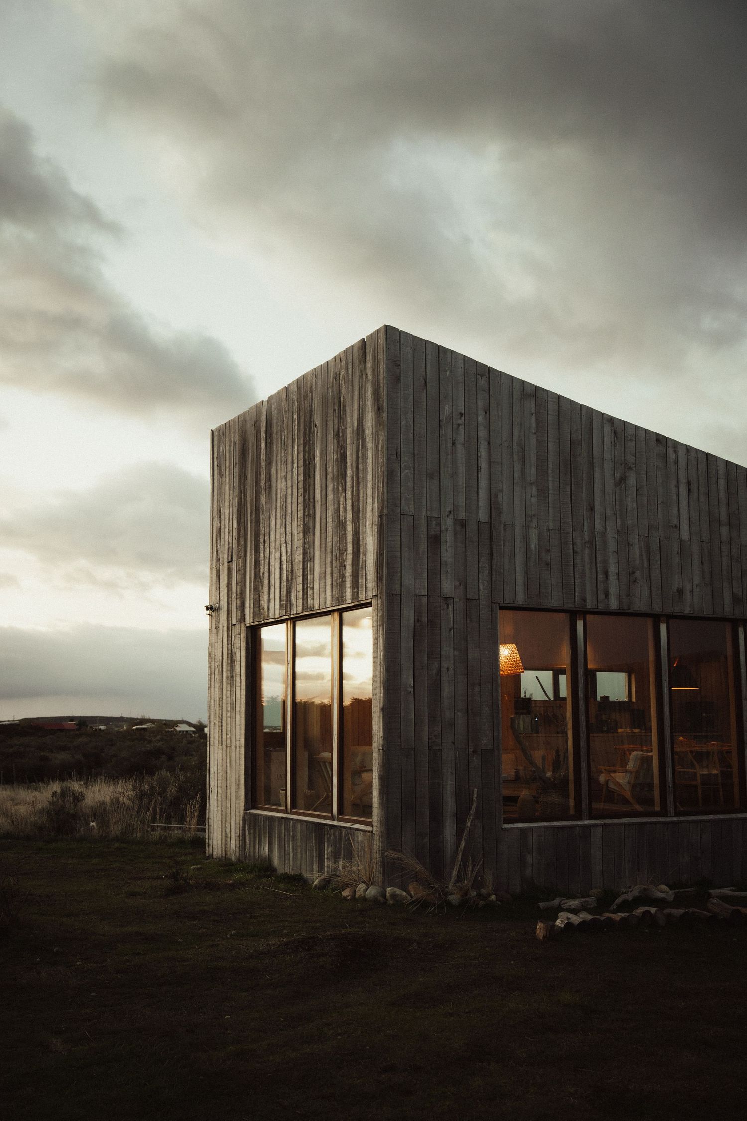 Weathered wooden barn or cabin with glowing windows at dusk under moody sky.