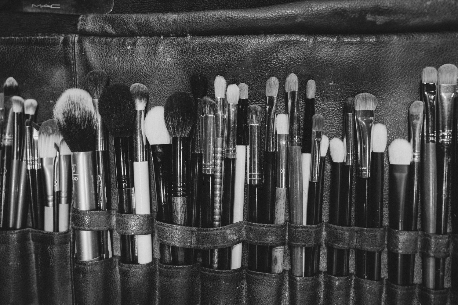 Black and white photo of a professional makeup brush set organized in a leather roll case.