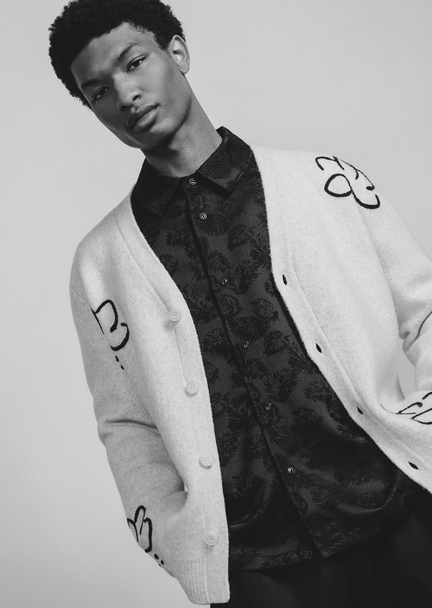 A black and white fashion portrait series showing someone in a white cardigan and dark shirt posing against a light background.