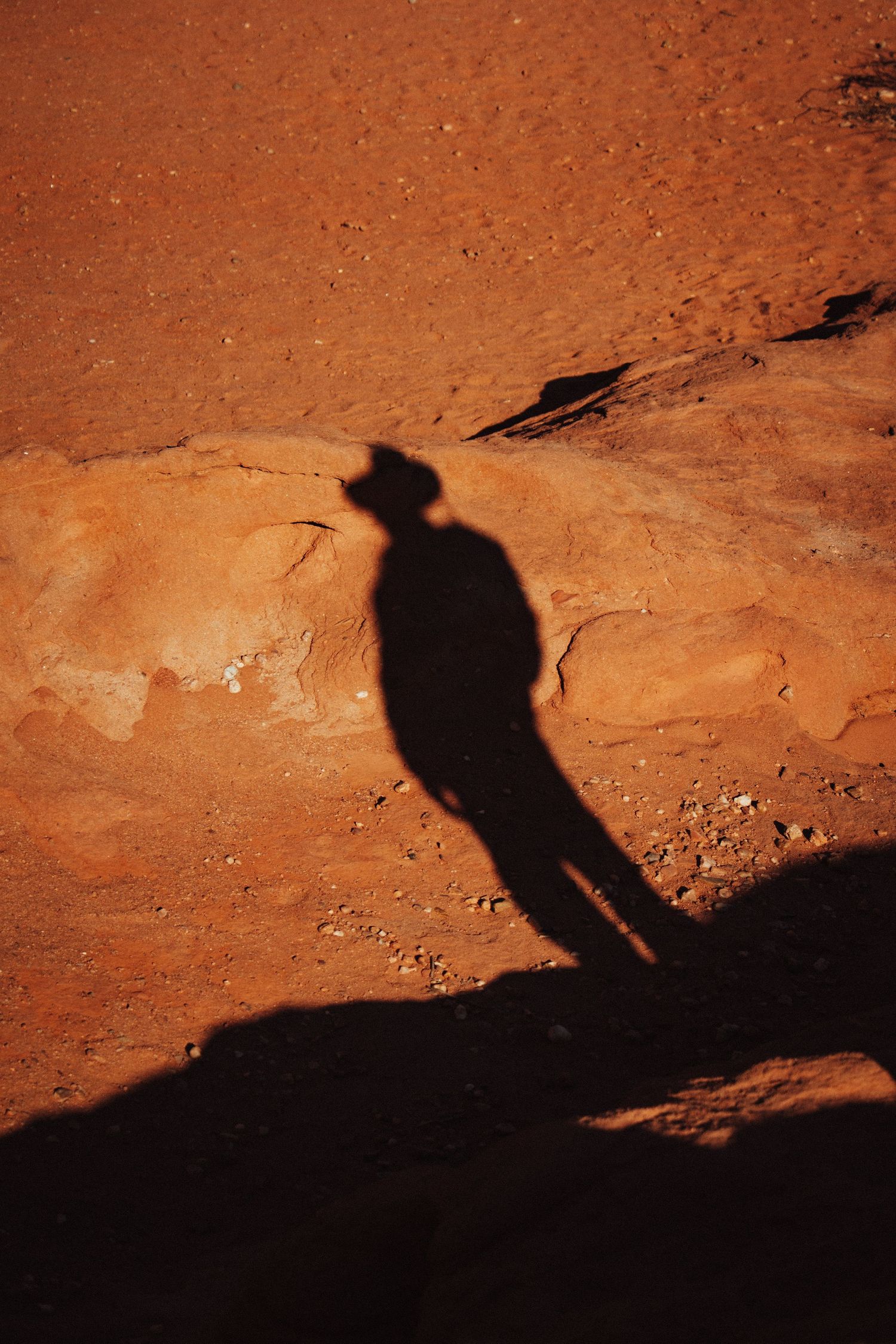 Shadow of a person wearing a cowboy hat cast on red desert rock.