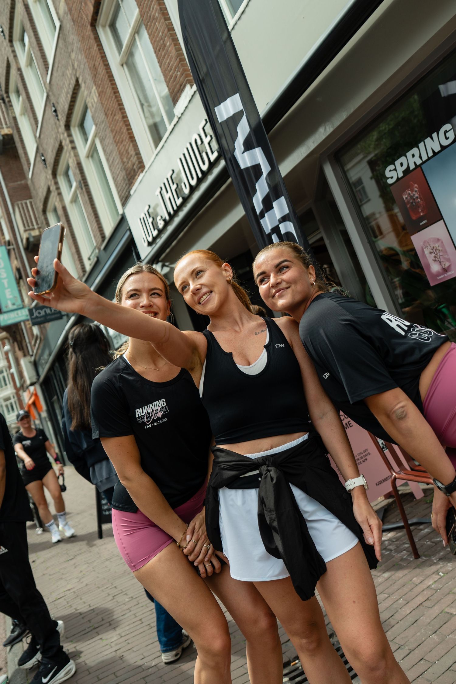 Three young women taking a selfie outside a juice bar on a sunny day.