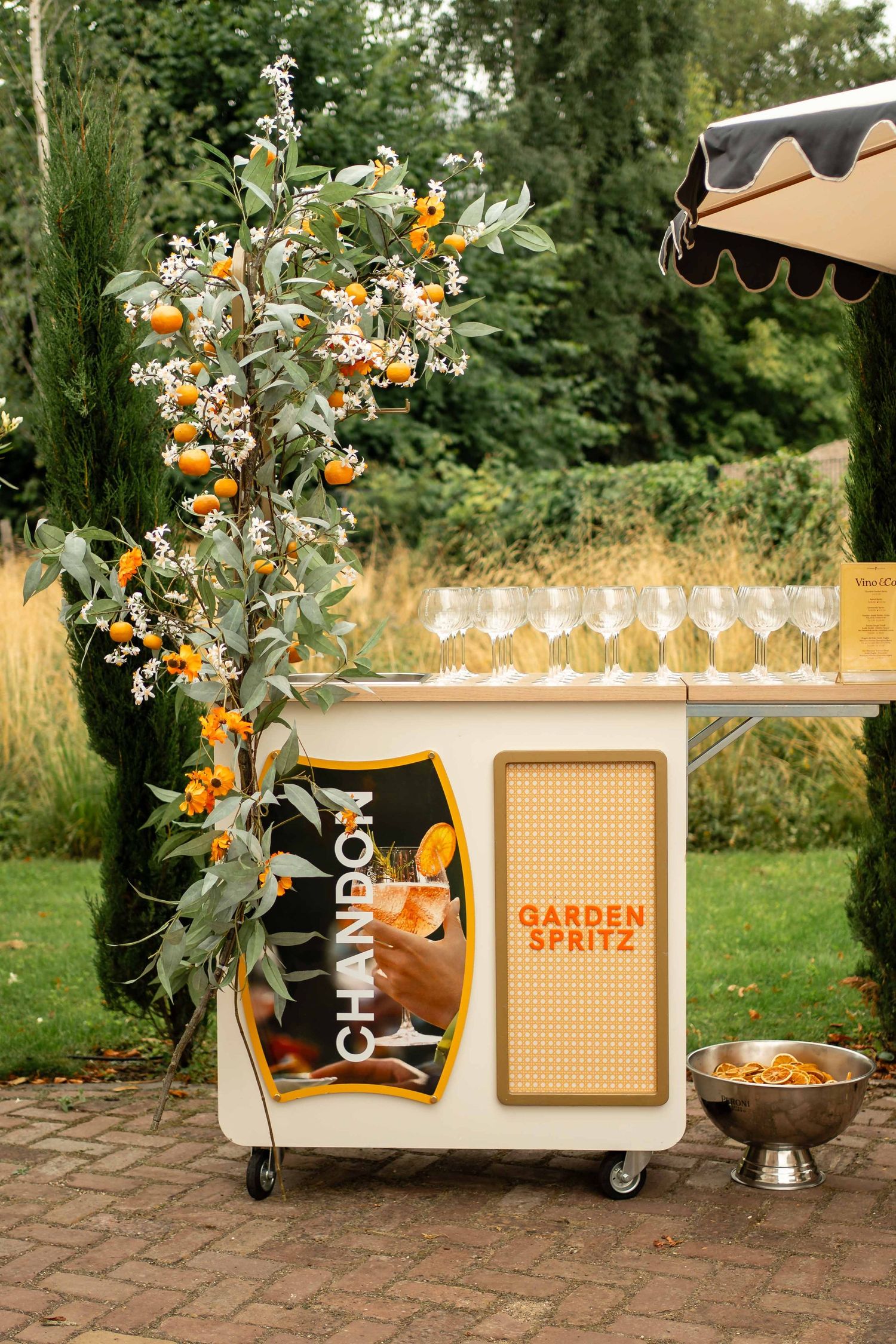 Chandon Garden Spritz outdoor bar cart with champagne flutes, orange floral decor, and lush greenery at an elegant event.