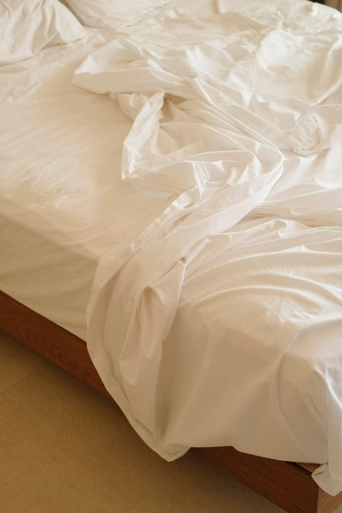 Unmade bed with wrinkled white sheets and duvet on a wooden bed frame.
