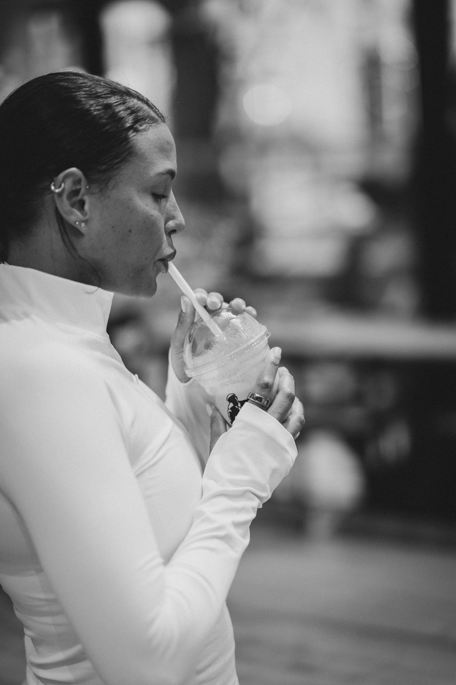 Black and white photo of a woman in a white turtleneck sipping a drink through a straw outdoors.