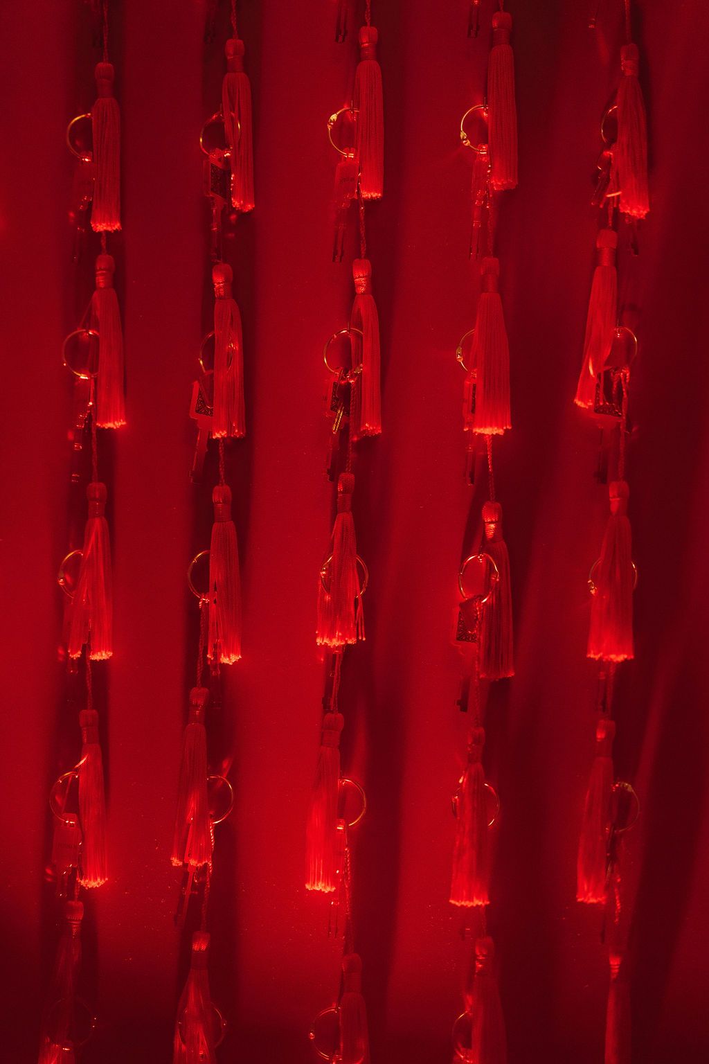 Red illuminated curtain with hanging glass bottle tassels and metal rings glowing in dramatic crimson light.