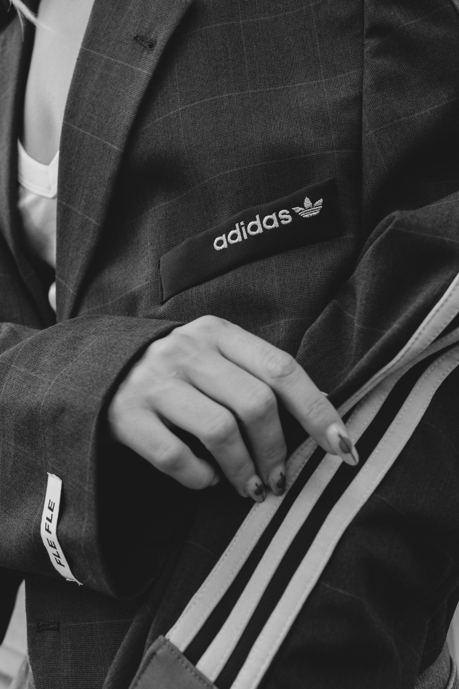 Black and white photo of a person wearing an Adidas branded suit jacket holding a striped bag.