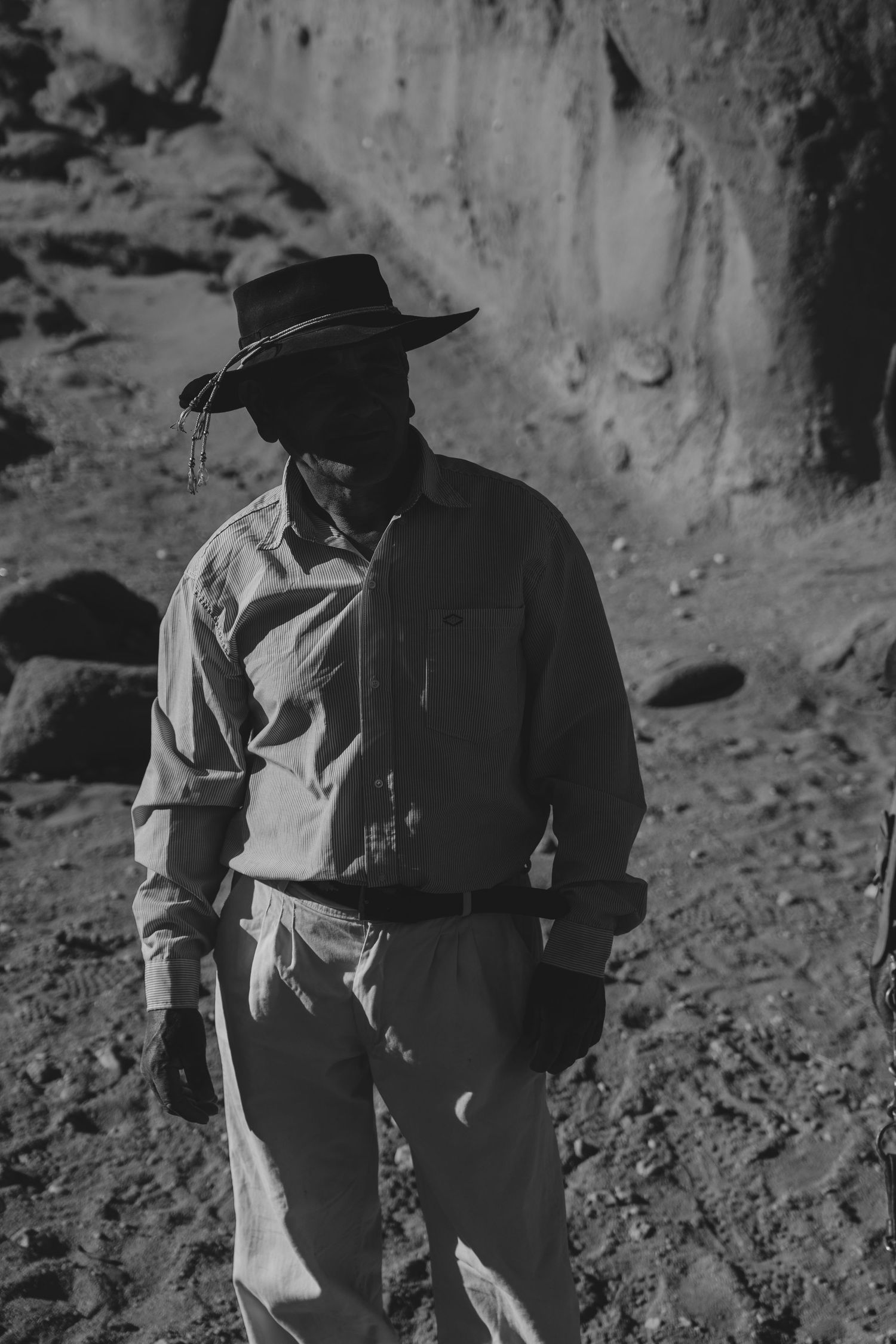 Two figures in western attire walking along a rocky cliff face in black and white.