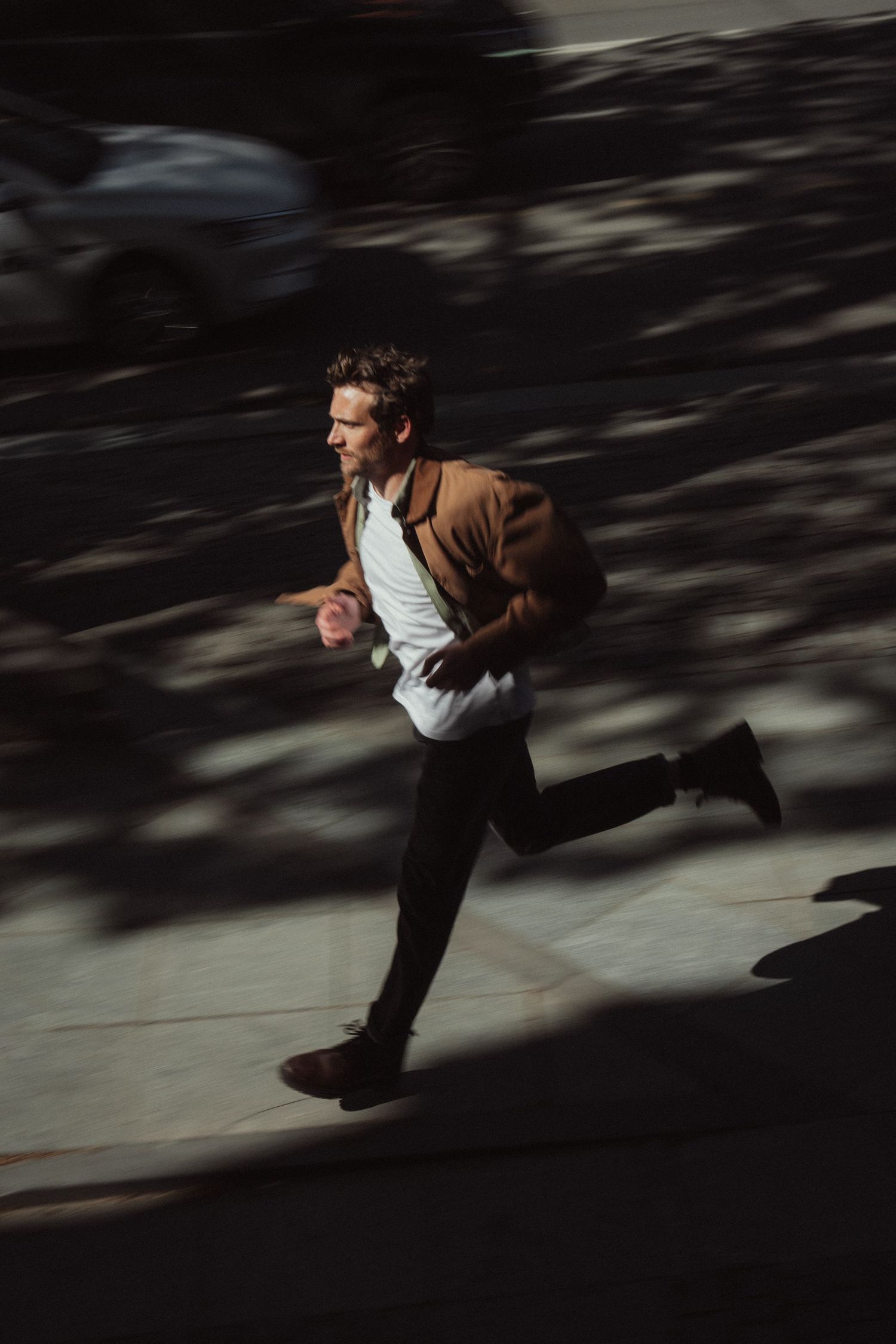 A person in a brown jacket and white shirt runs through a dark space creating a motion blur effect.