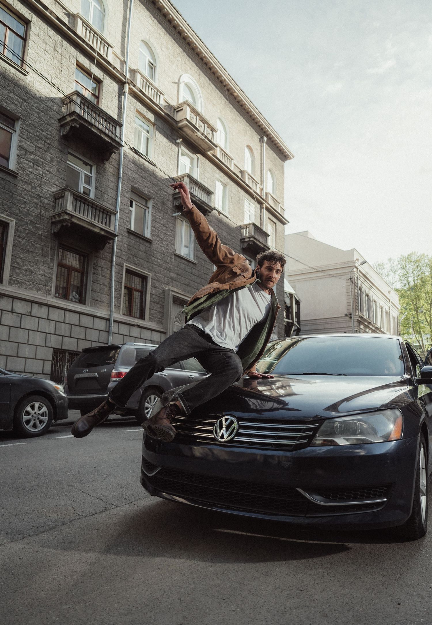 Person performs dramatic poses on a black Volkswagen car parked on a city street.