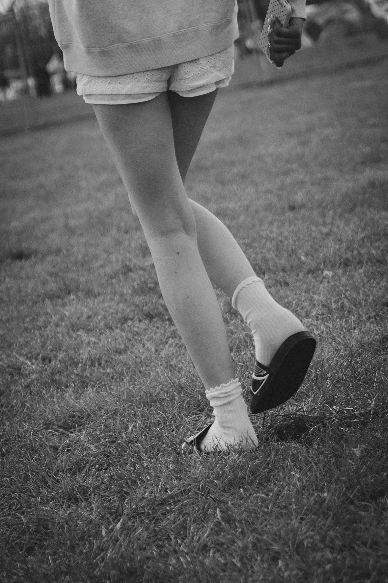 Black and white photo of a person walking on grass wearing Nike shoes, white socks, and shorts.