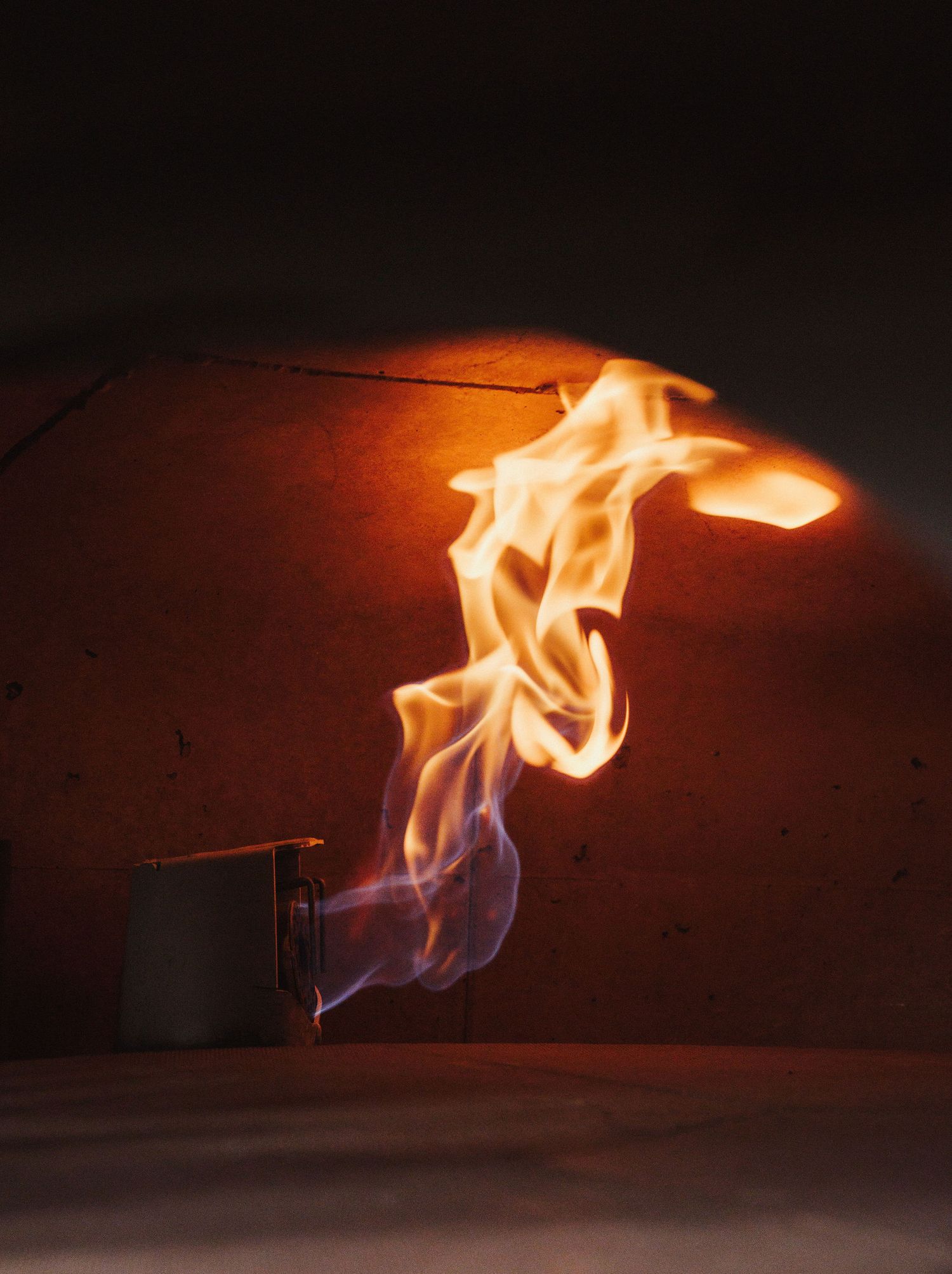 Vibrant orange and blue flames dancing inside a traditional wood-fired brick pizza oven with glowing ember light.