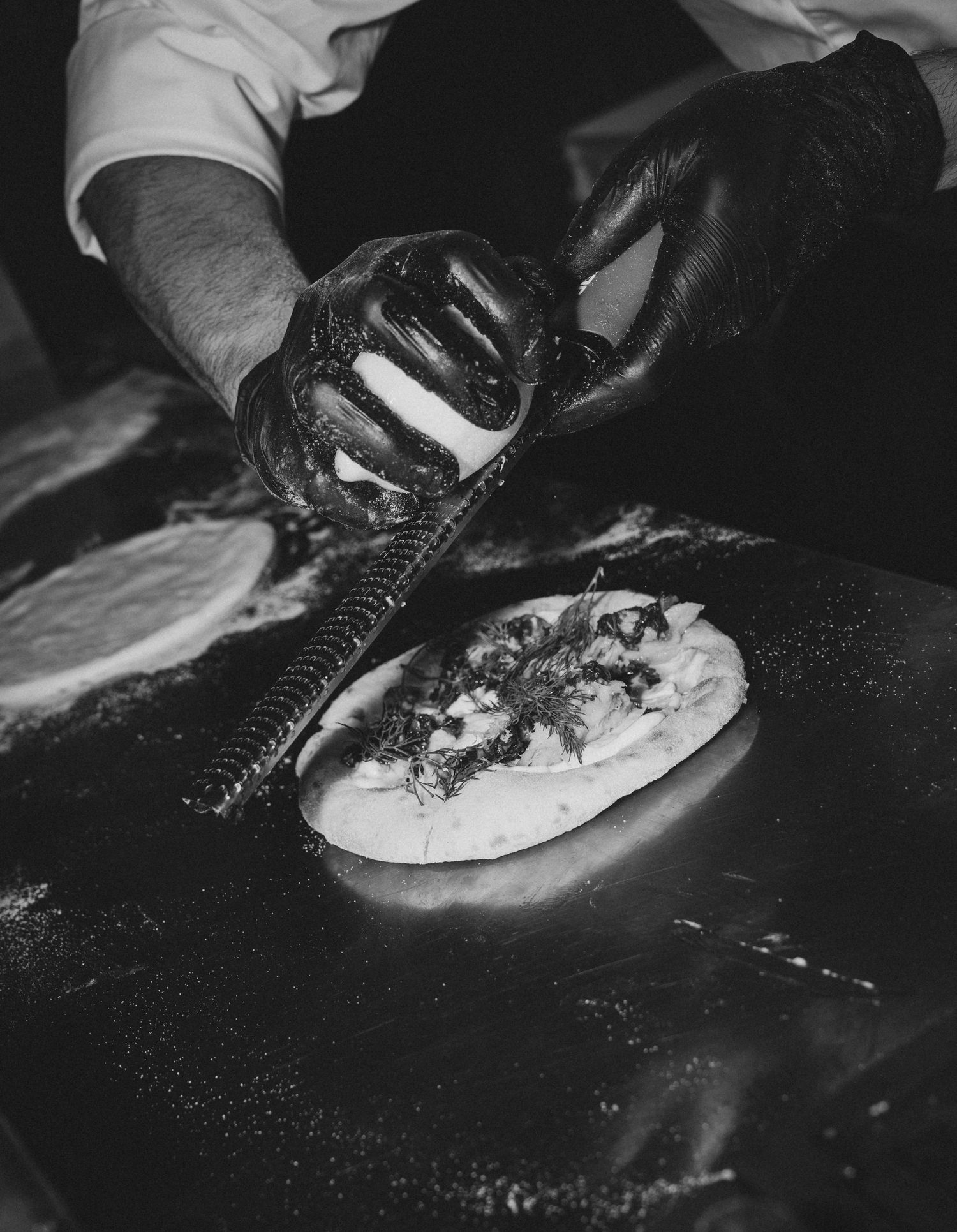 Chef in black gloves using a squeeze bottle to garnish a flatbread on a hot griddle.
