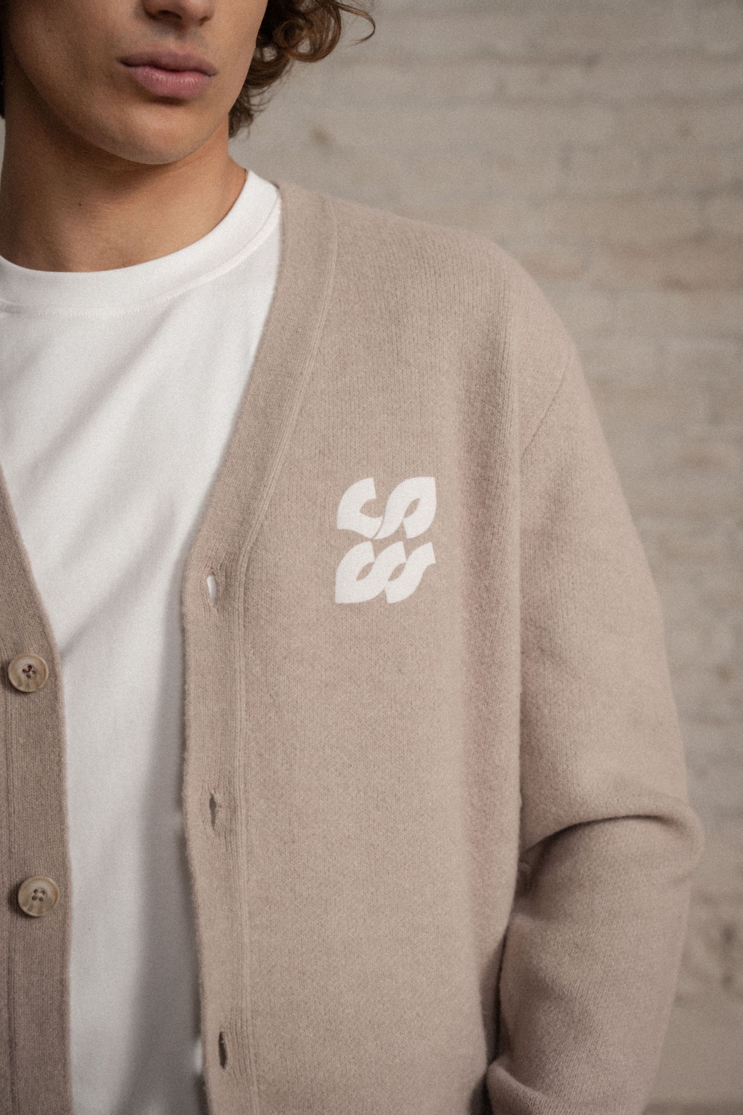 Close-up view of a beige cardigan sweater with white t-shirt detail showing texture and button closure.
