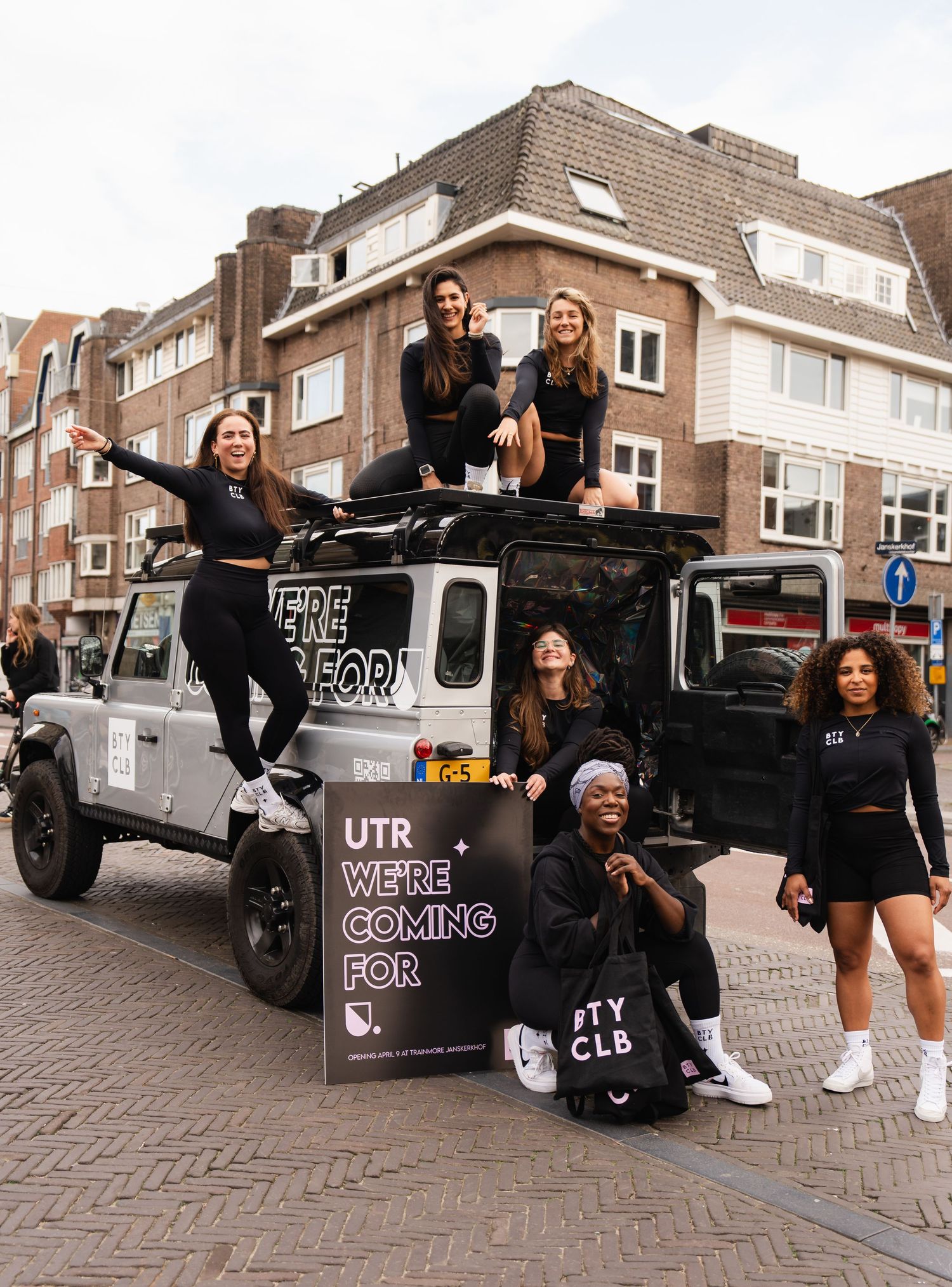 Group of women in black outfits posing on and around a Jeep with UTR signage on a city street.