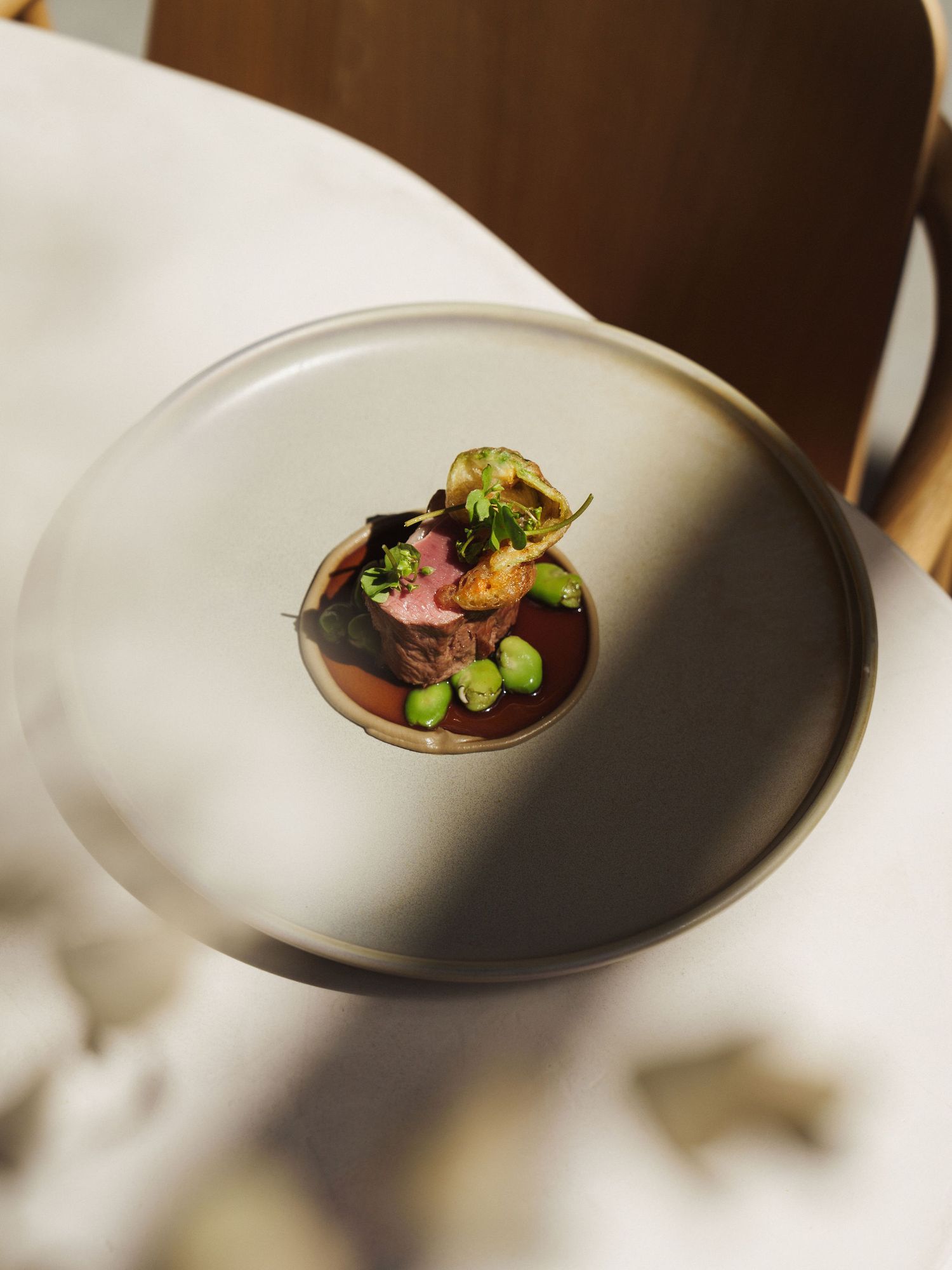 Elegant fine dining dish with pink meat, edamame, and garnish in rich sauce on a matte gray plate.
