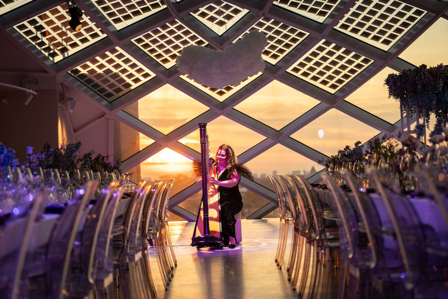 Harpist performing at sunset in an elegant venue with geometric ceiling and purple lighting.