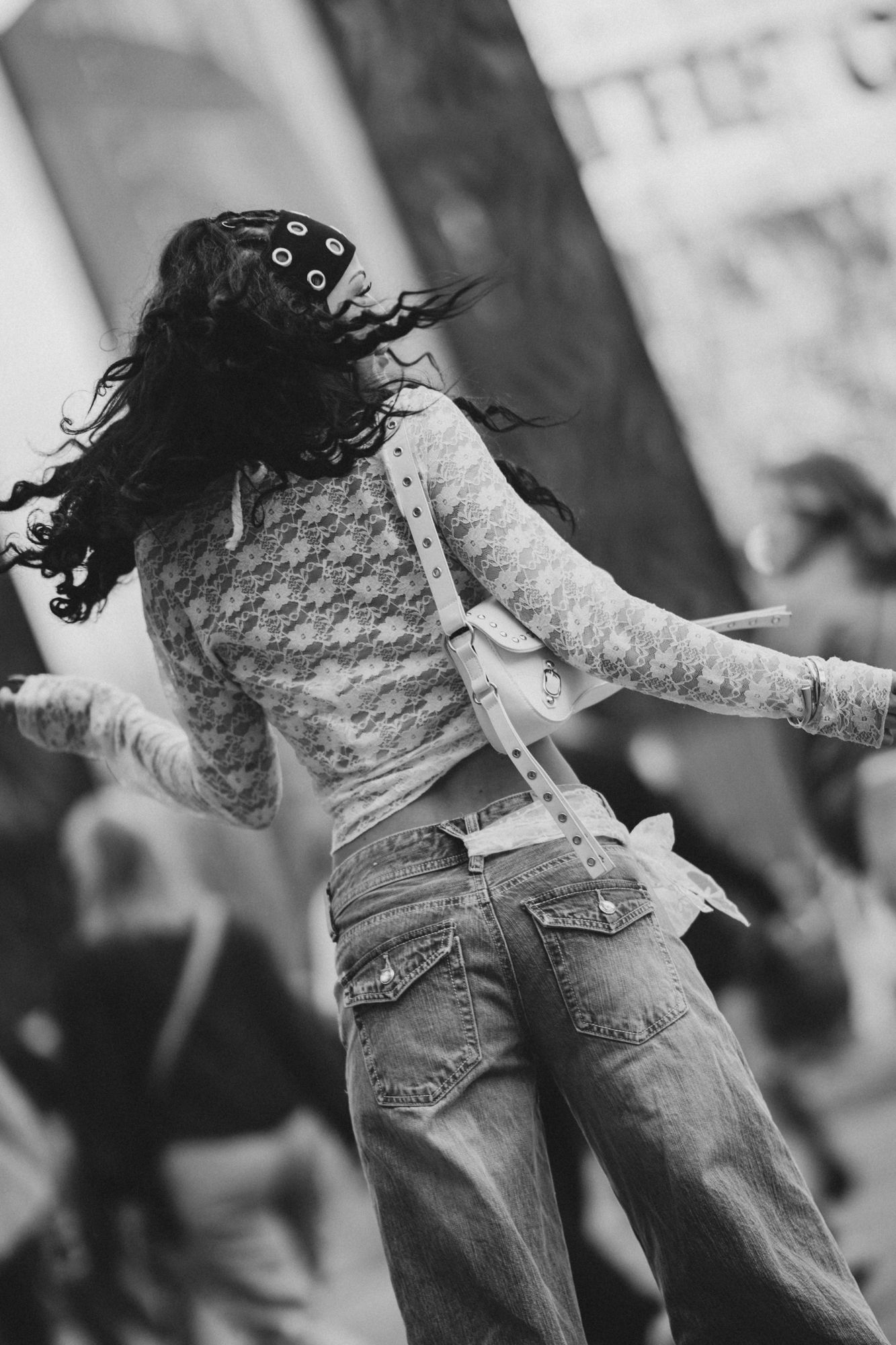 Black and white photo of a woman dancing outdoors, wearing lace top and jeans, hair flowing in the wind.