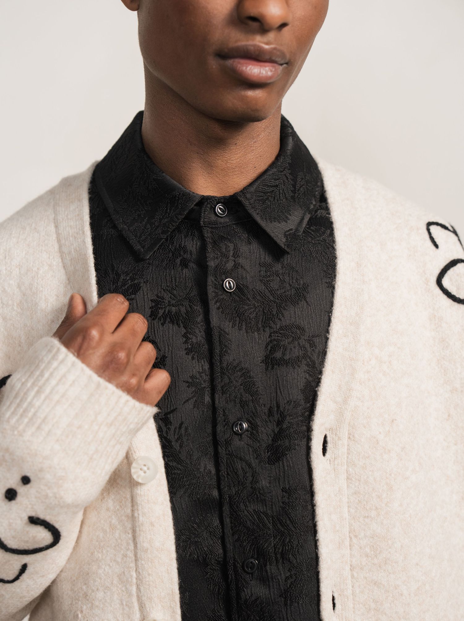 Fashion model wearing a white knit sweater with black floral embroidered collar detail against neutral background.