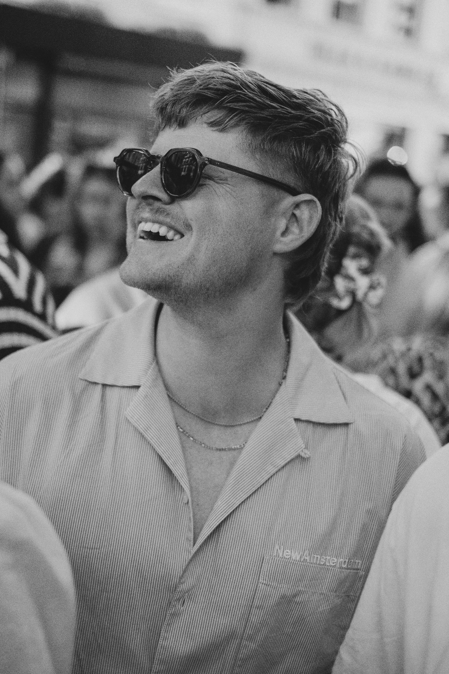 Person in sunglasses and light colored shirt smiling at outdoor event in black and white.