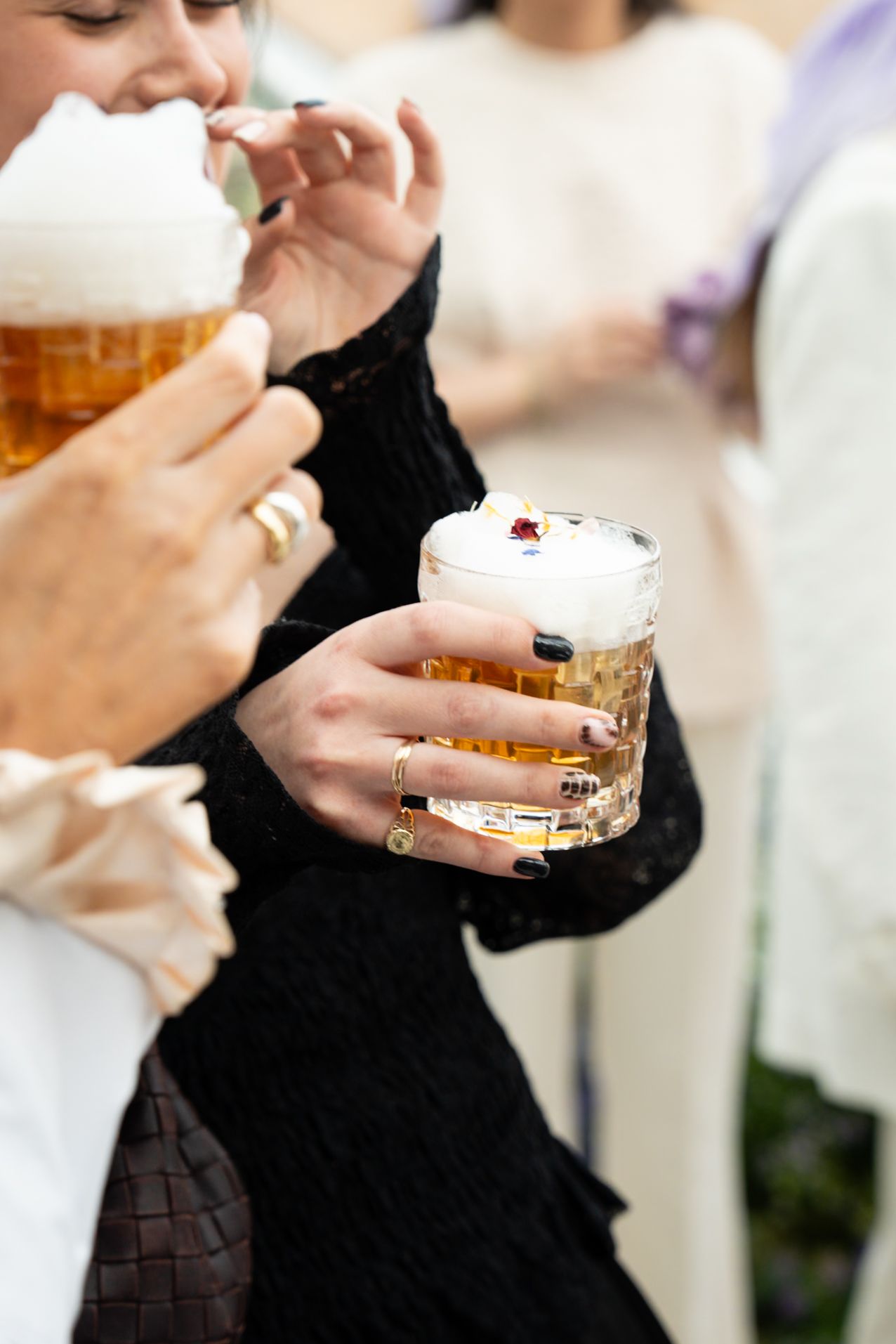 Women holding frothy beer glasses with decorative foam at social gathering event.