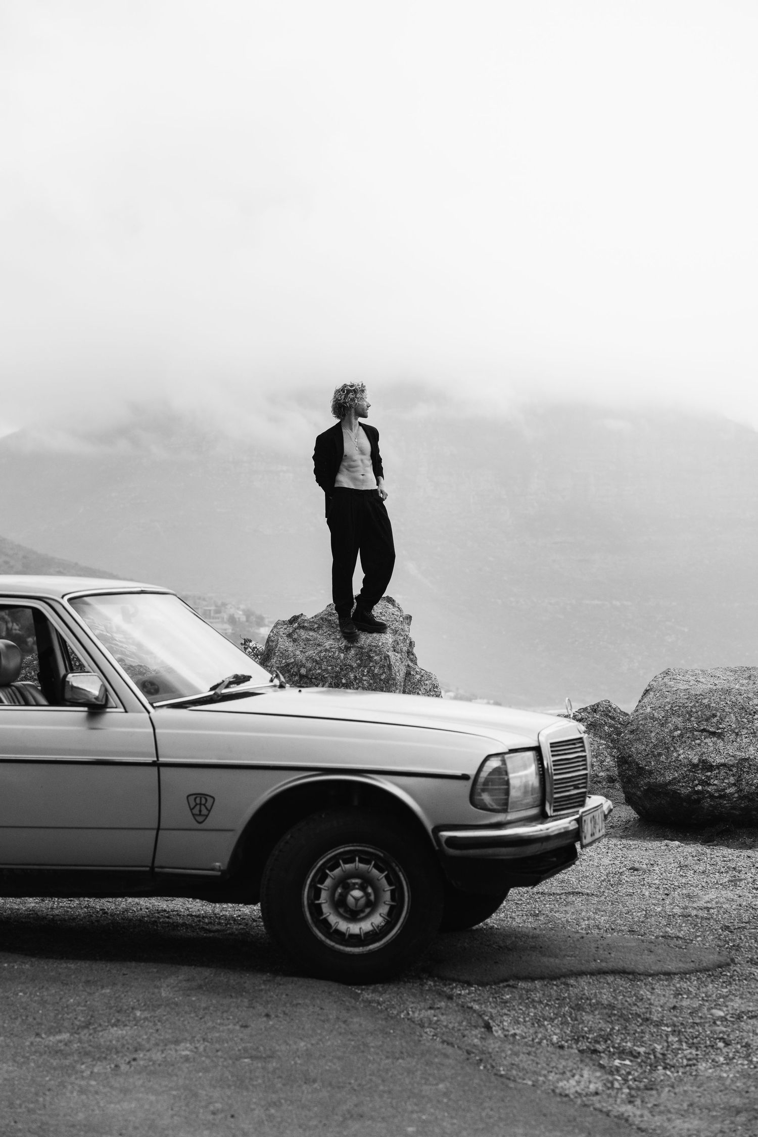 Classic Mercedes car parked on hilltop with figure silhouetted against sky.