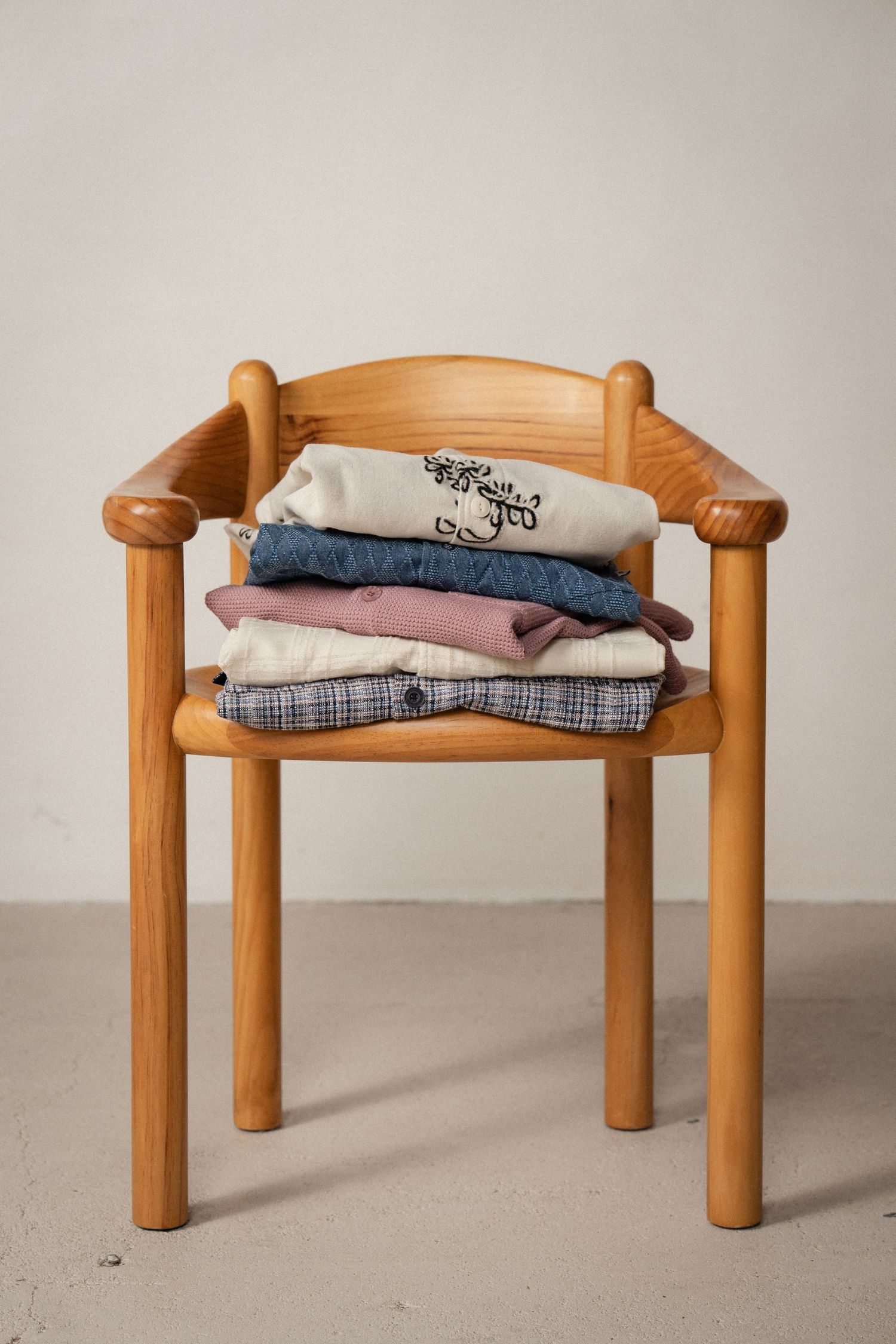 Wooden bench with curved posts displays neatly folded clothing items in a minimalist setting.